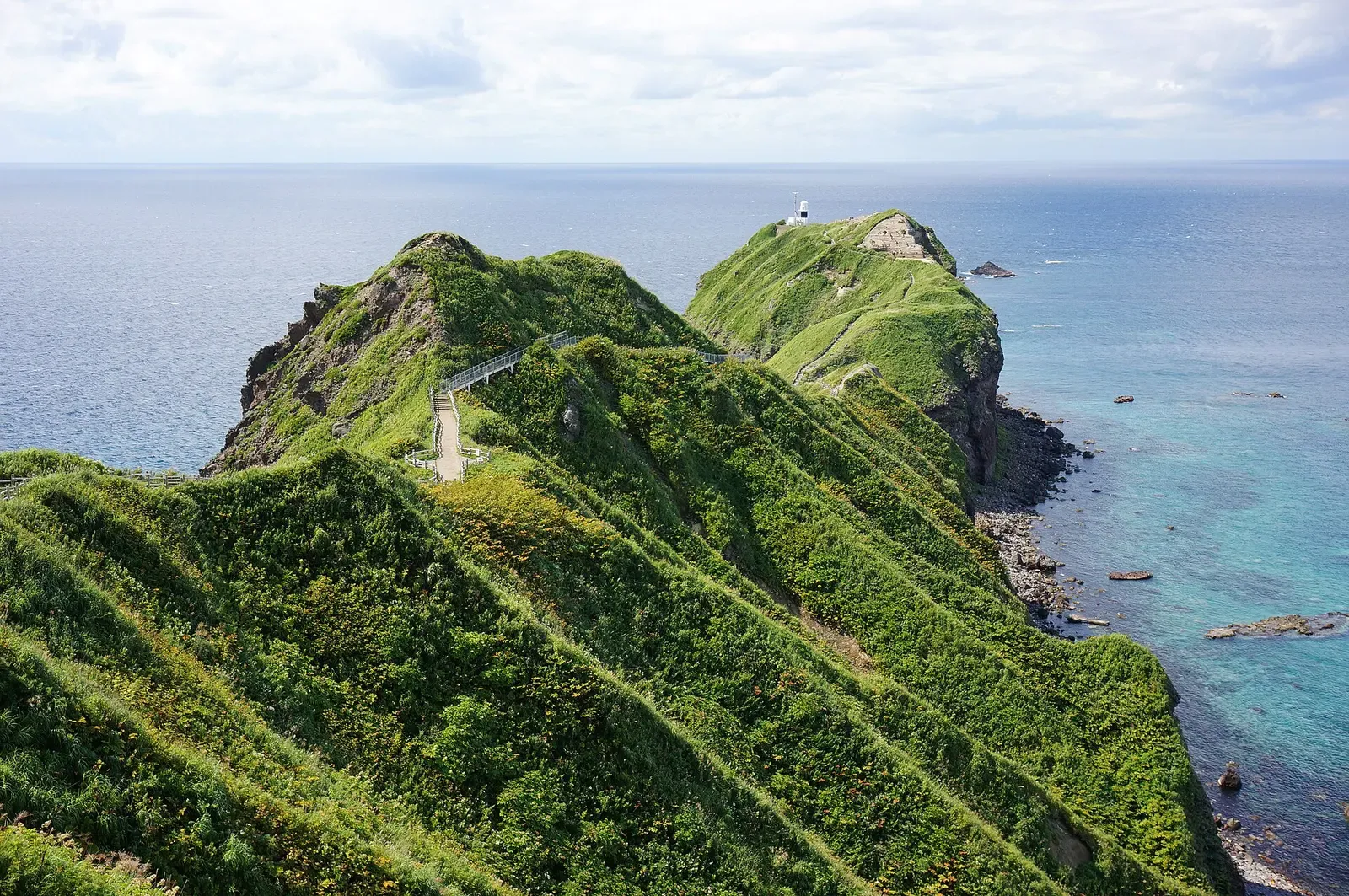 Green grass-covered headland of Cape Kamui running out into blue sea under a hazy sky — Shakotan Peninsula