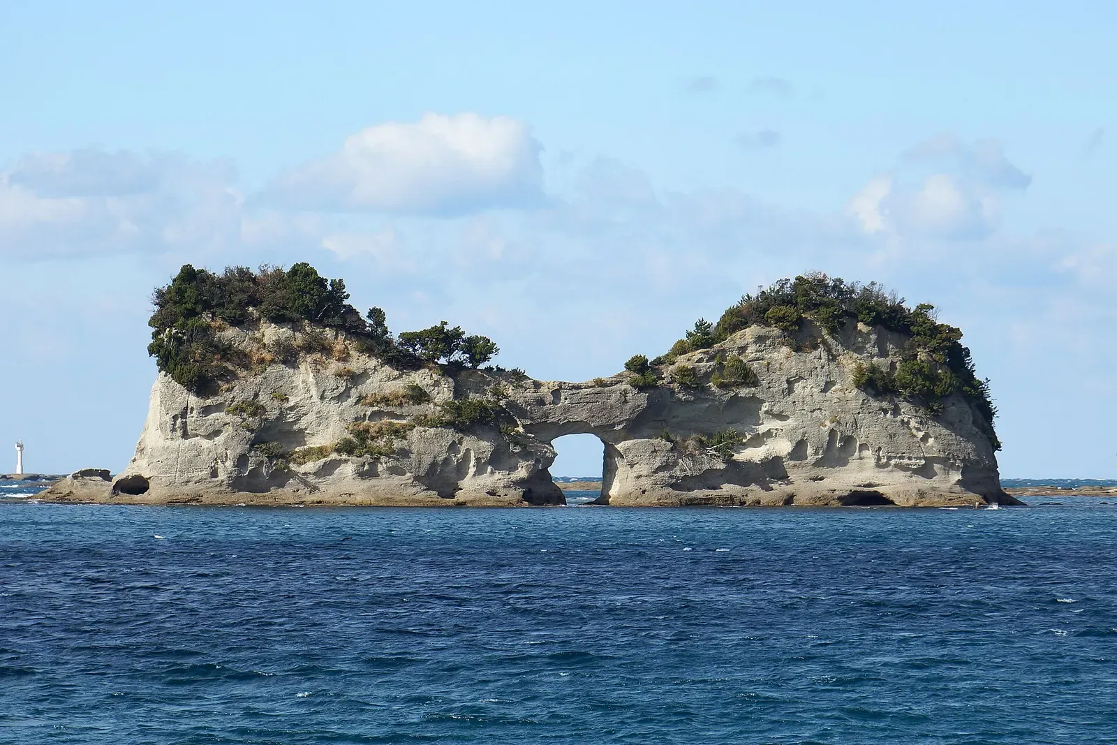 Engetsu Island, a pale sandstone islet with a sea arch through its middle and pine-topped crests, in deep blue water under a light blue sky — Nanki-Shirahama & Tanabe