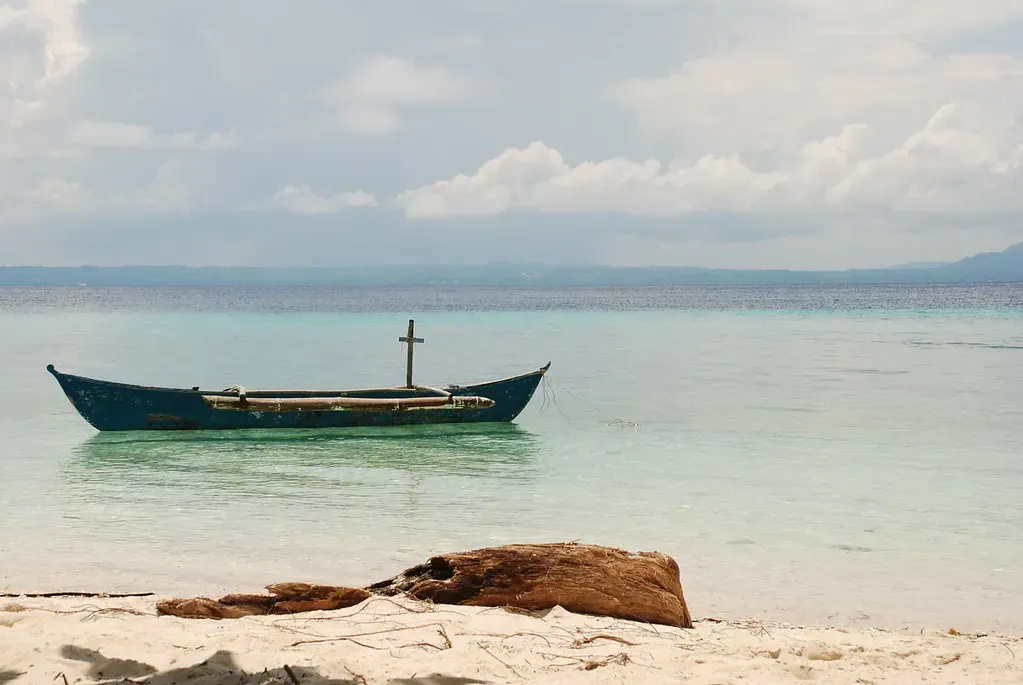 An outrigger rests on Pamilacan's white sand with pale turquoise shallows beyond