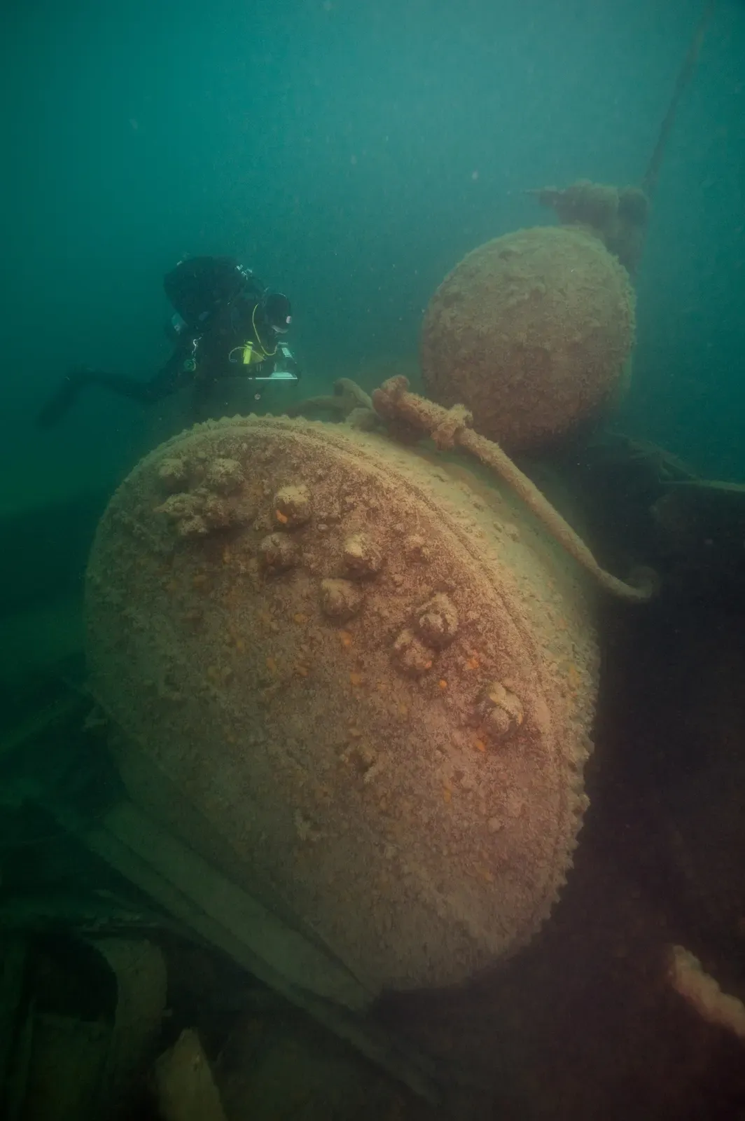 One scuba diver in green water above two large round rust-brown pieces of wreckage — SS George M. Cox, Isle Royale.