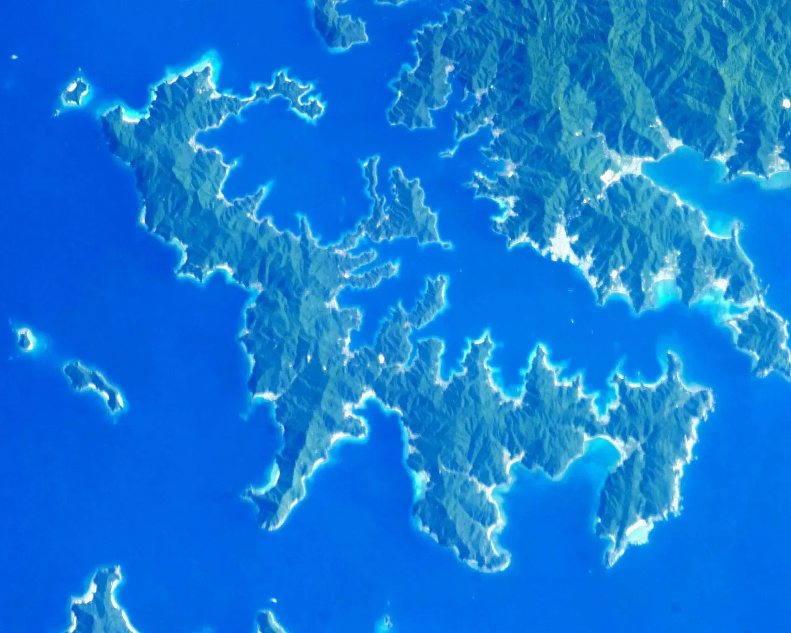 Astronaut photograph of Kakeroma Island's deeply indented green coastline in deep blue sea — Amami Ōshima