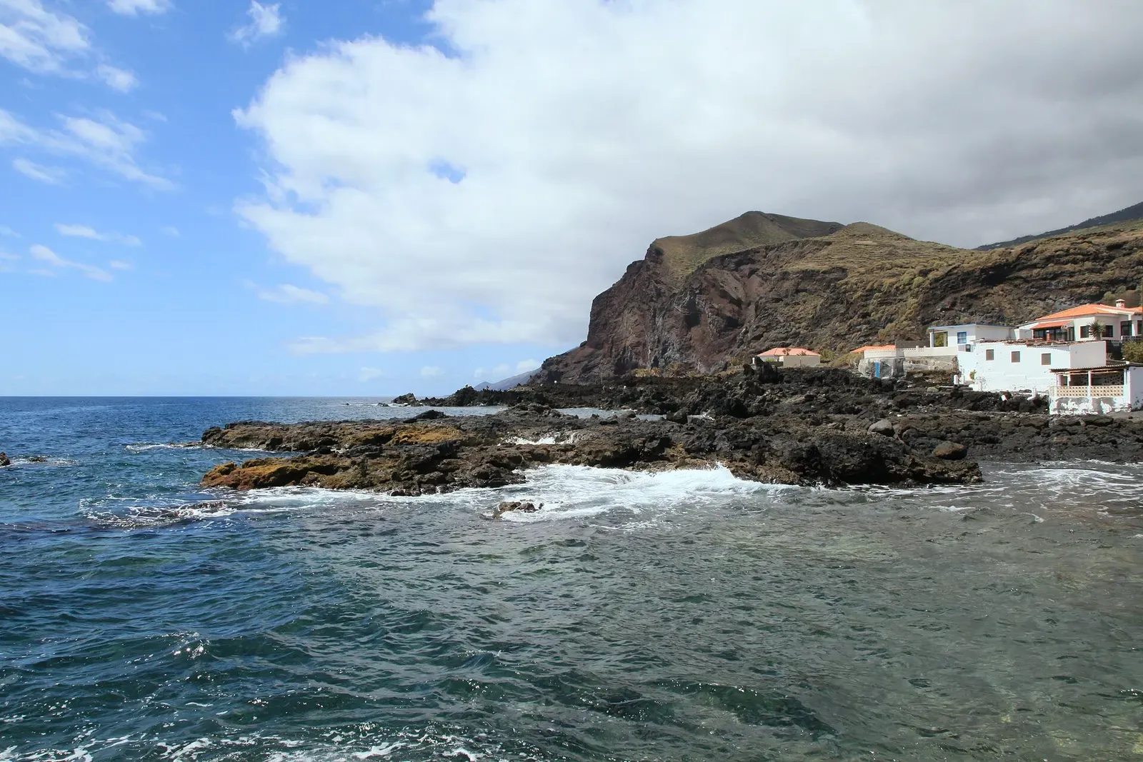 Waves break over black volcanic rocks below cliffs on La Palma's rugged south coast