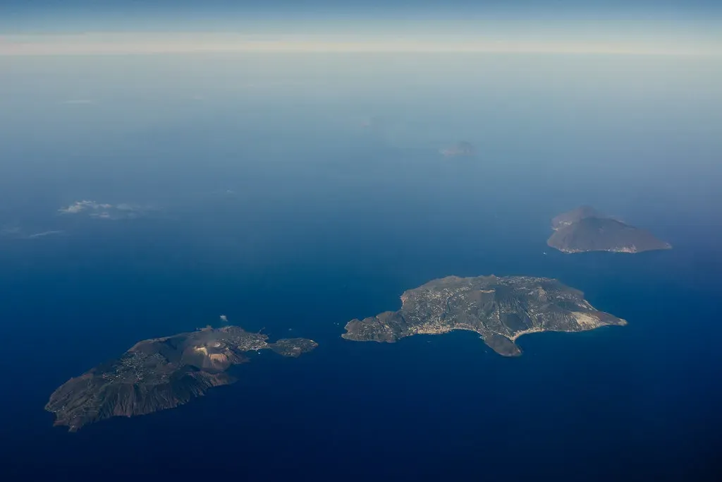 Aerial view of several small volcanic islands scattered across deep blue sea under a thin haze — Filicudi & Salina