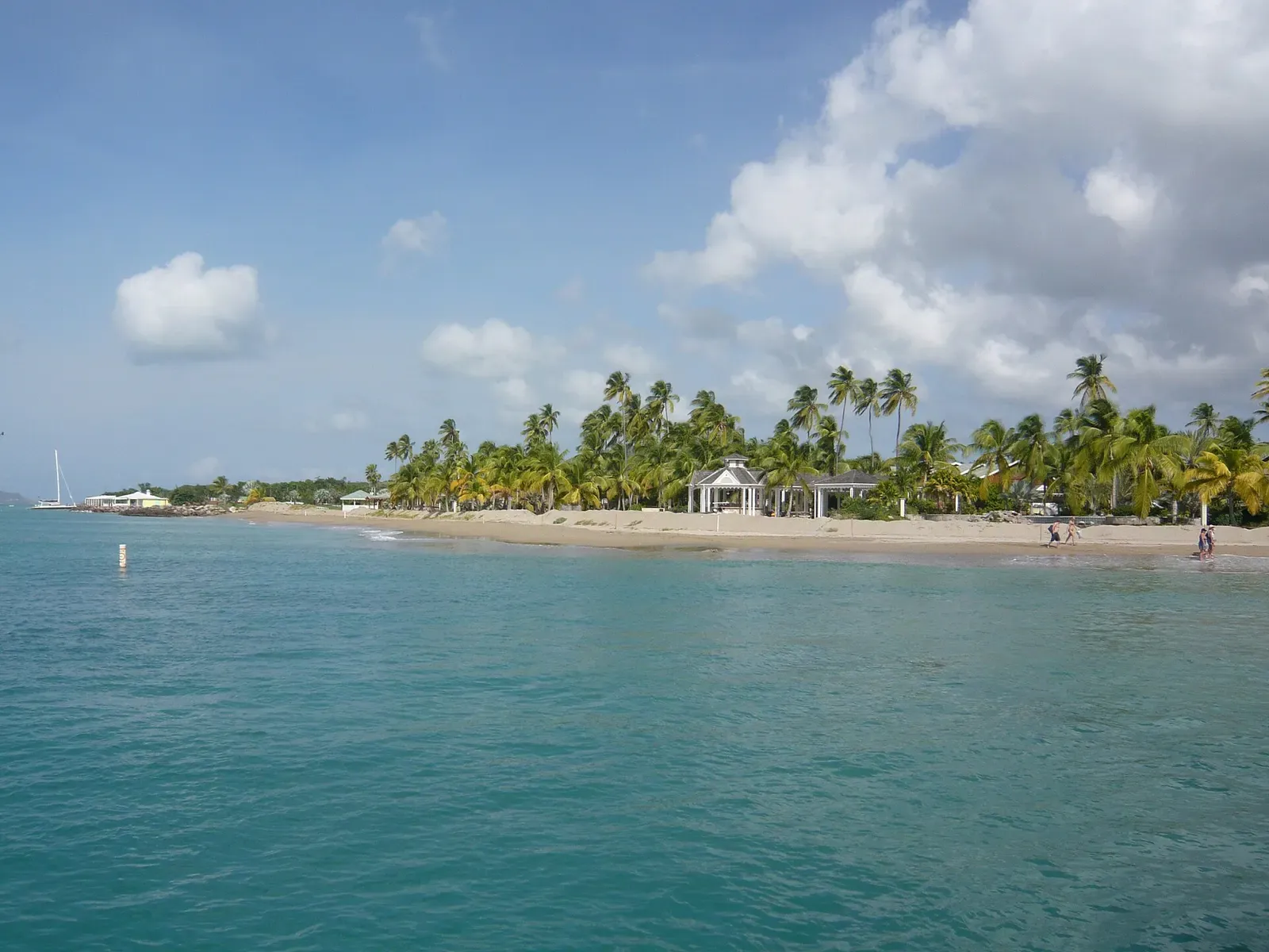 Turquoise shallow water off a palm-lined sand beach with two white gazebos and a few people at the waterline — Nevis
