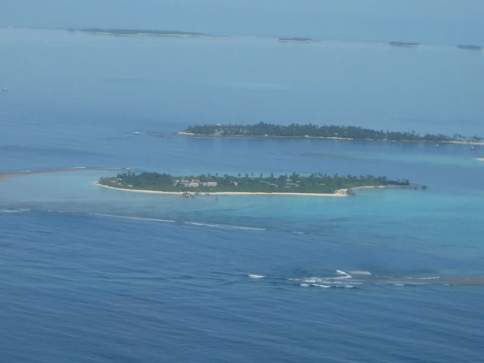 Aerial view of a narrow, palm-covered island ringed by a turquoise lagoon in Laamu Atoll