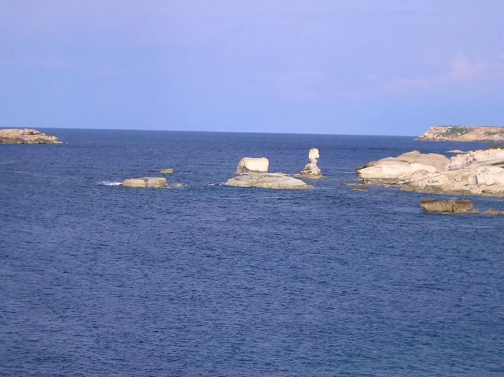 Pale limestone rocks and sea stacks rise from a calm, deep blue sea under a clear sky — Paphos & Coral Bay.