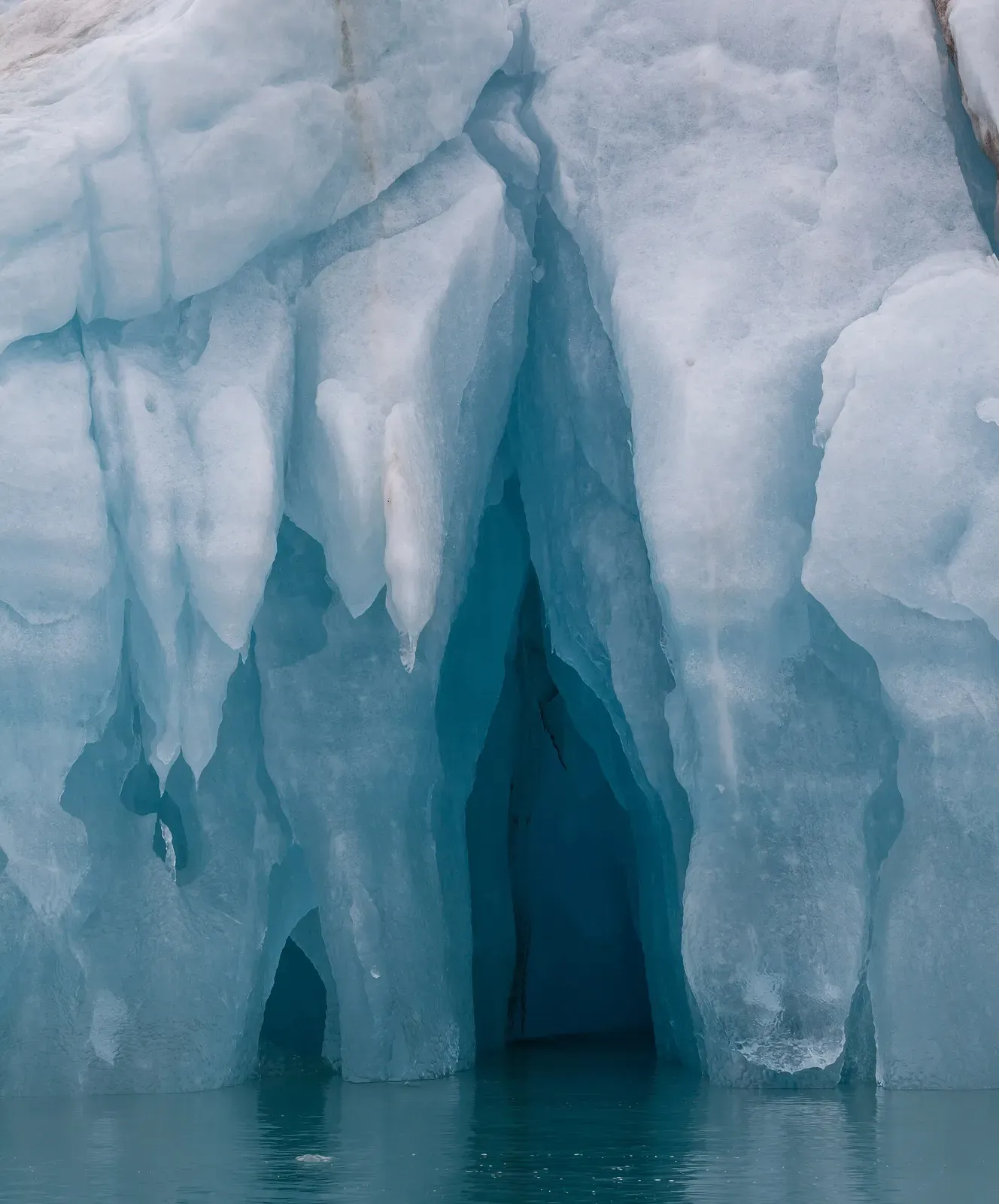 A carved blue ice cave opening at the waterline of an iceberg in Liefdefjord — Svalbard