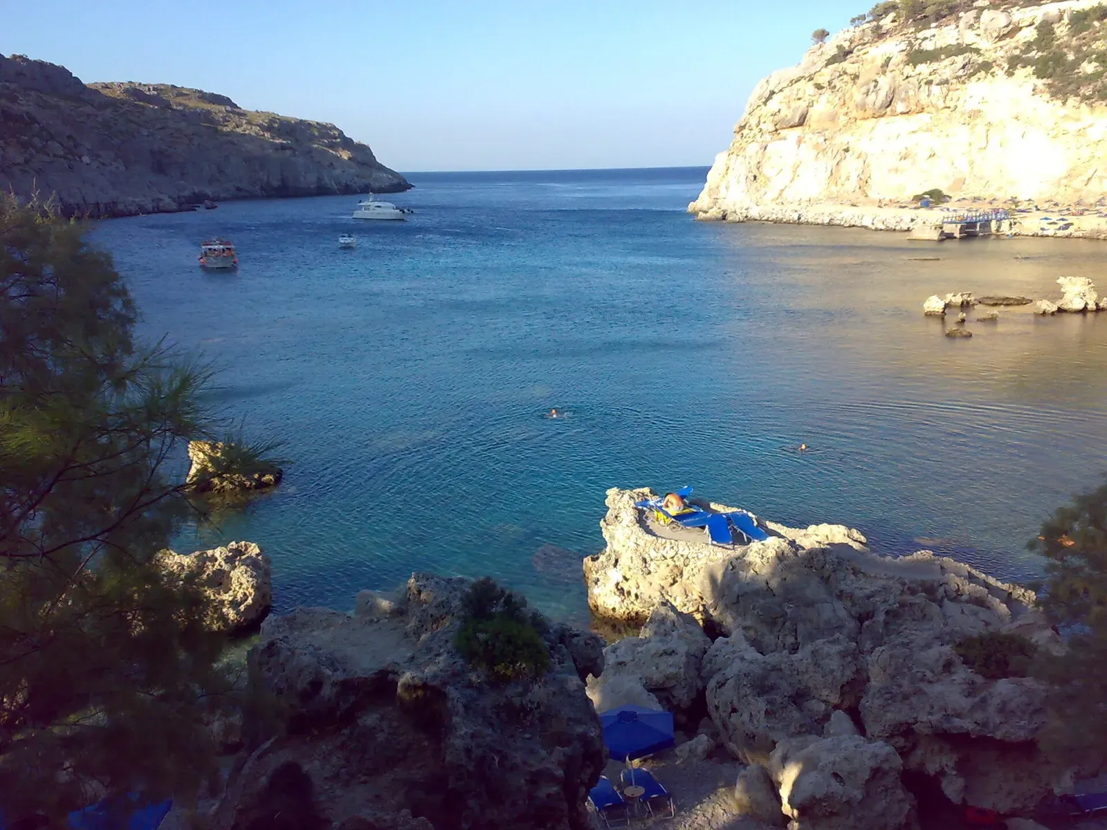 Wide view of Anthony Quinn Bay's cliffs and turquoise water at sunset