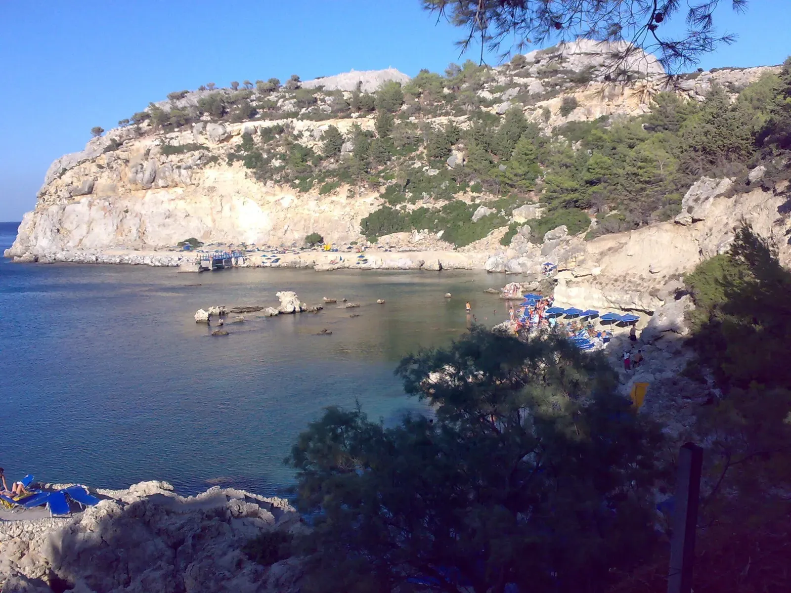 Aerial view of Anthony Quinn Bay's rocky cove with boats anchored in clear water