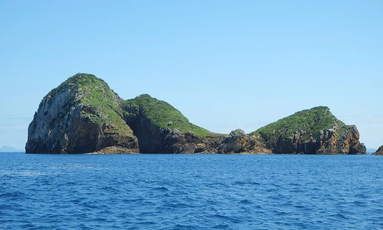 Archway Island seen from the northeast, its rock arch entrance visible in silhouette on the left — Blue Maomao Arch, Poor Knights Islands.
