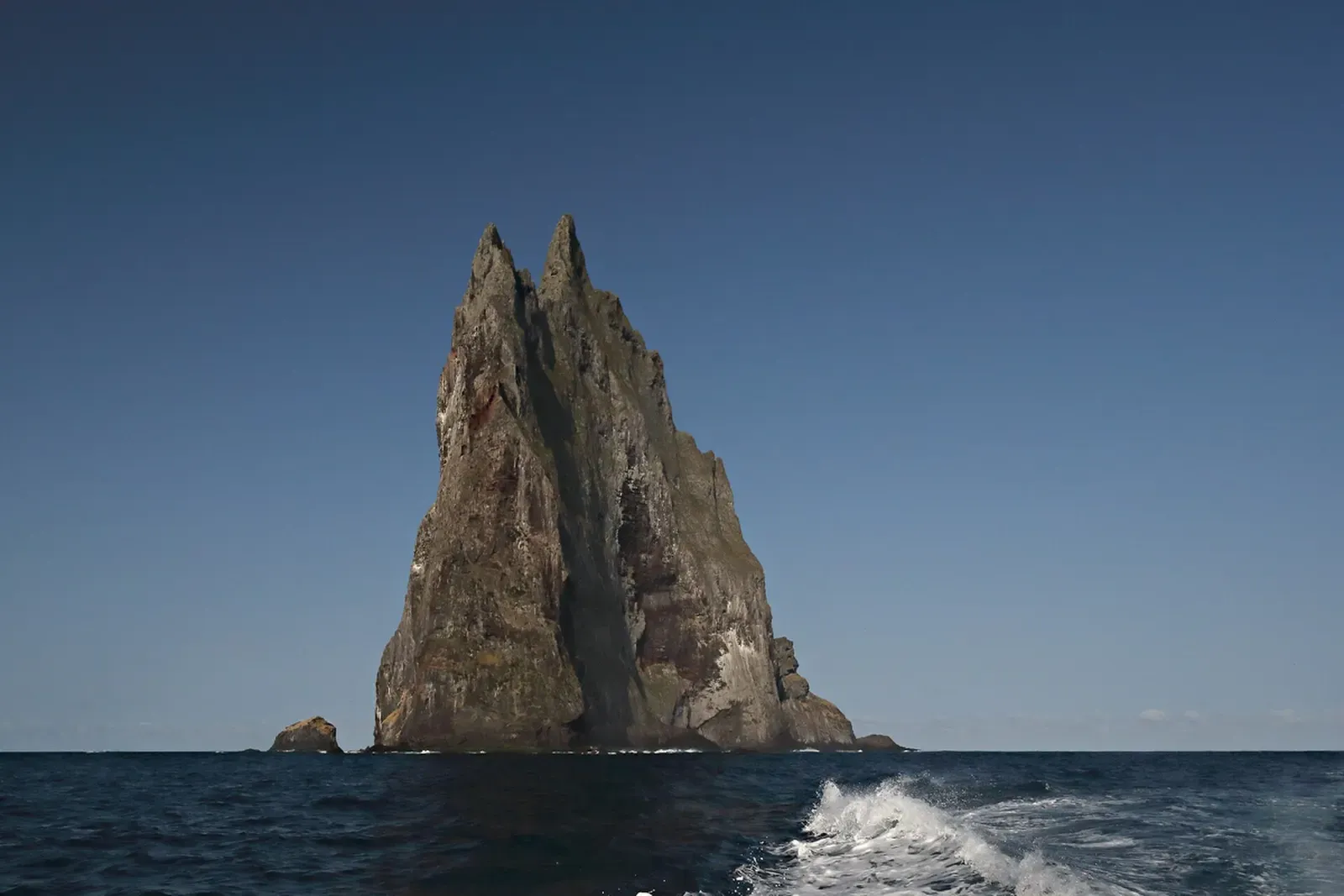 Twin-peaked Ball's Pyramid seen from a boat, wake trailing in the foreground — Balls Pyramid, Lord Howe Island