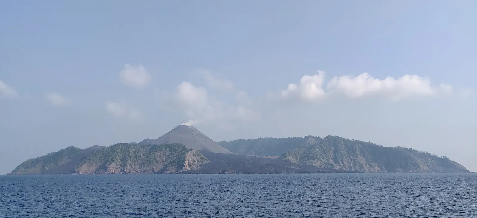Barren Island's volcanic cone rising above the sea, seen from a boat with haze around the summit — Andaman Islands