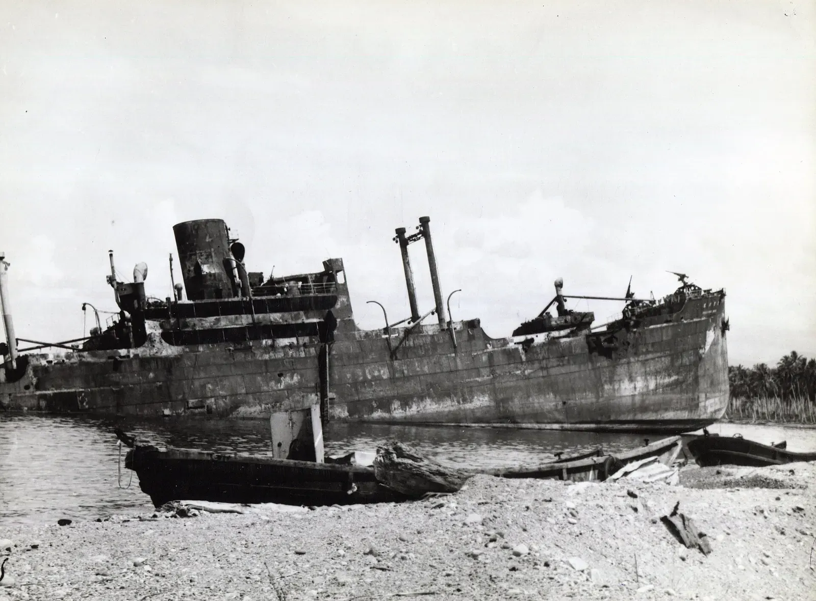 Side view of the riddled, beached hull of the Kinugawa Maru resting on the shore — Bonegi II, Iron Bottom Sound