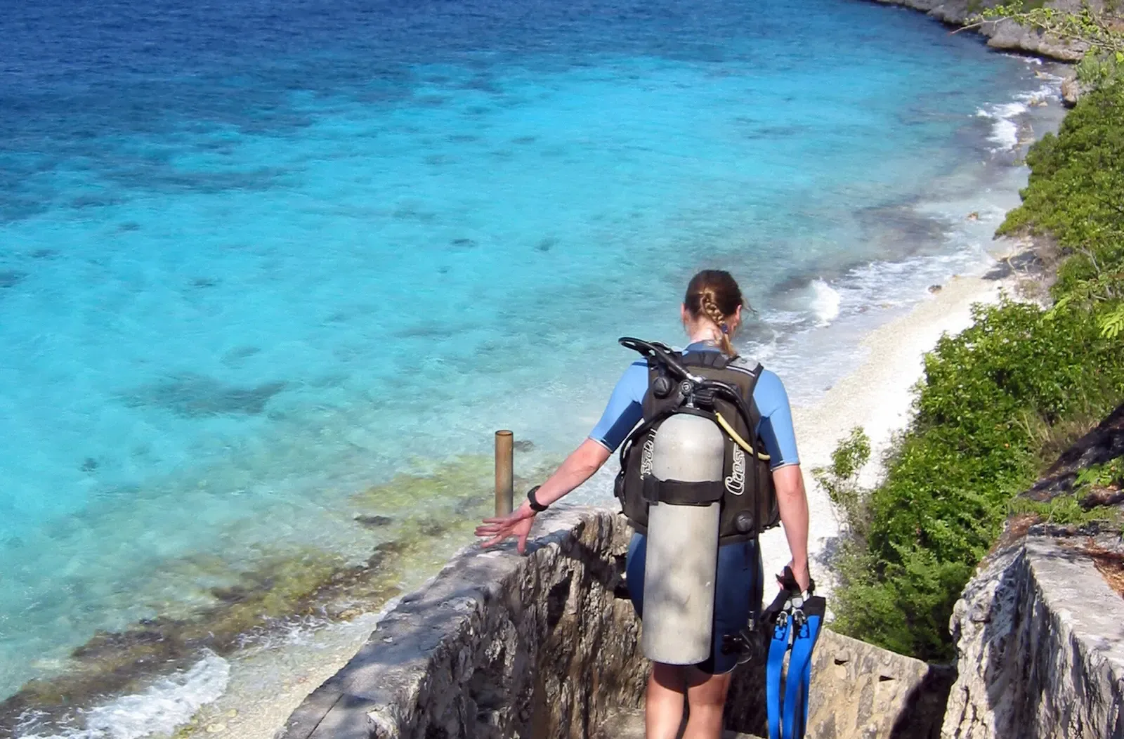 Diver in full scuba gear descending the stone steps toward turquoise water — 1000 Steps, Bonaire