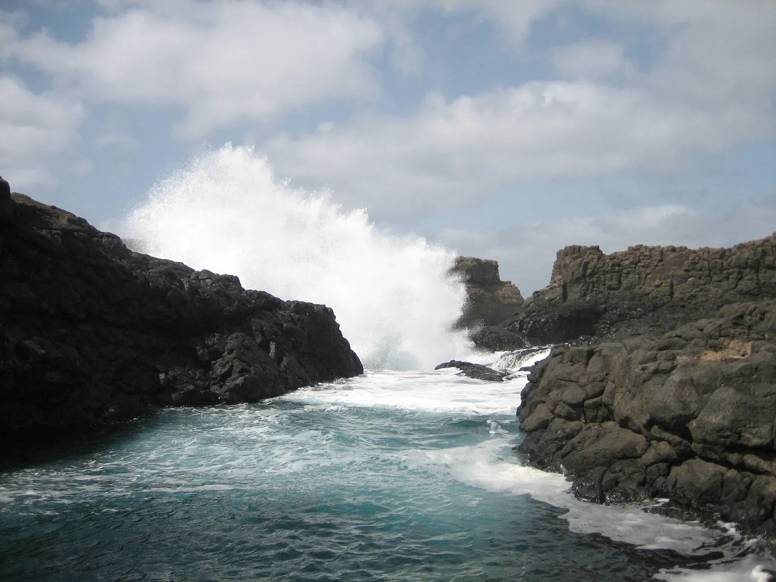 Waves breaking through the black volcanic rock arch at Buracona, Sal