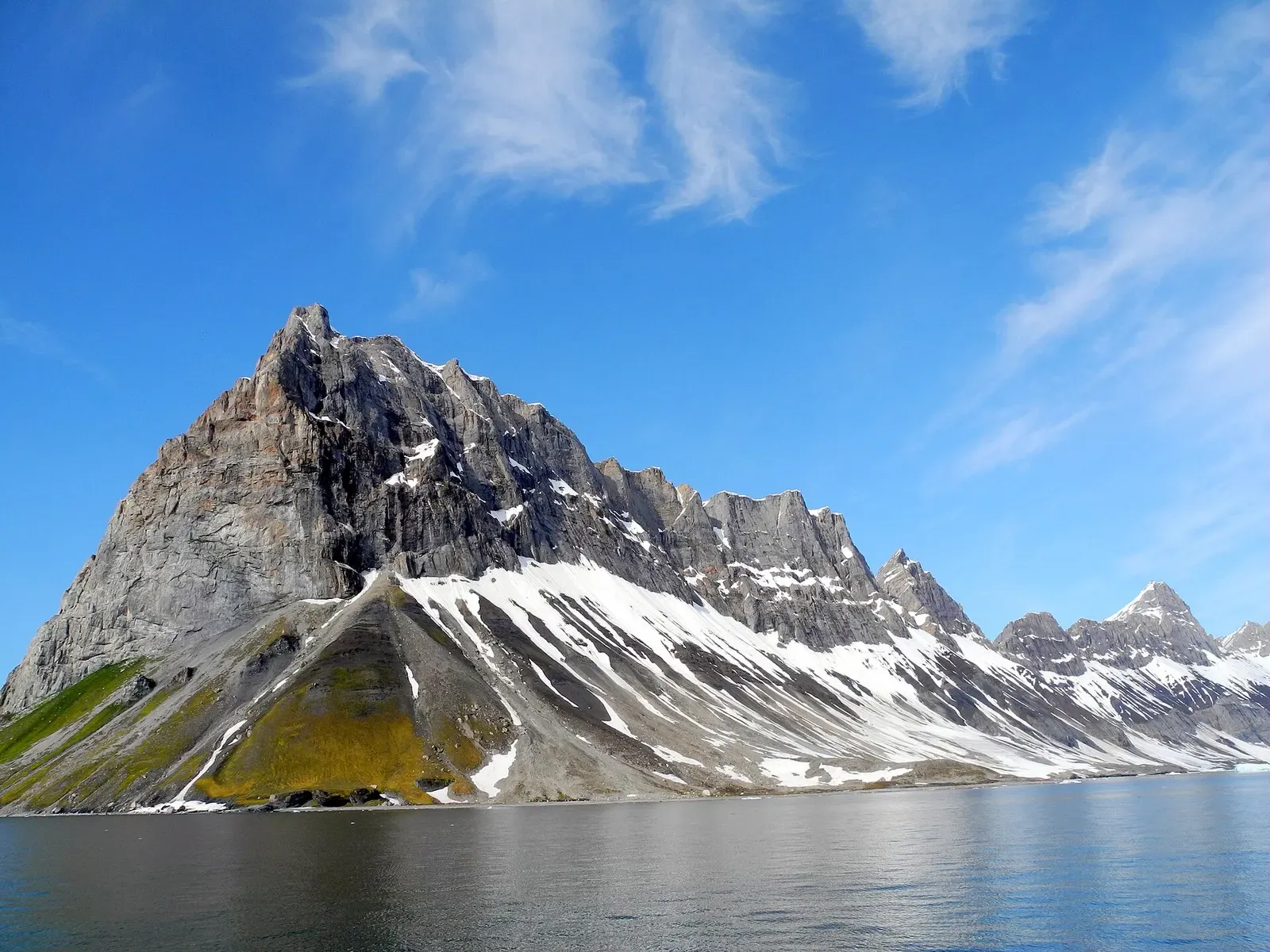 Snow-streaked mountain peak reflected in the still water of Burgerbukta, a bay inside Hornsund — Svalbard.
