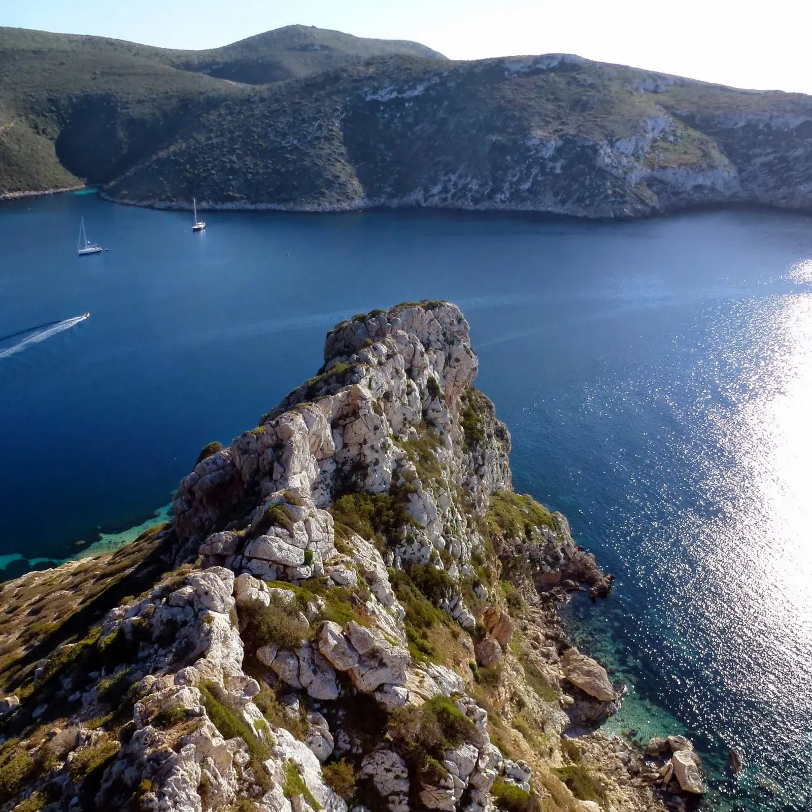 Limestone ridge dropping into clear blue water with sailboats anchored beyond — Cabrera Archipelago