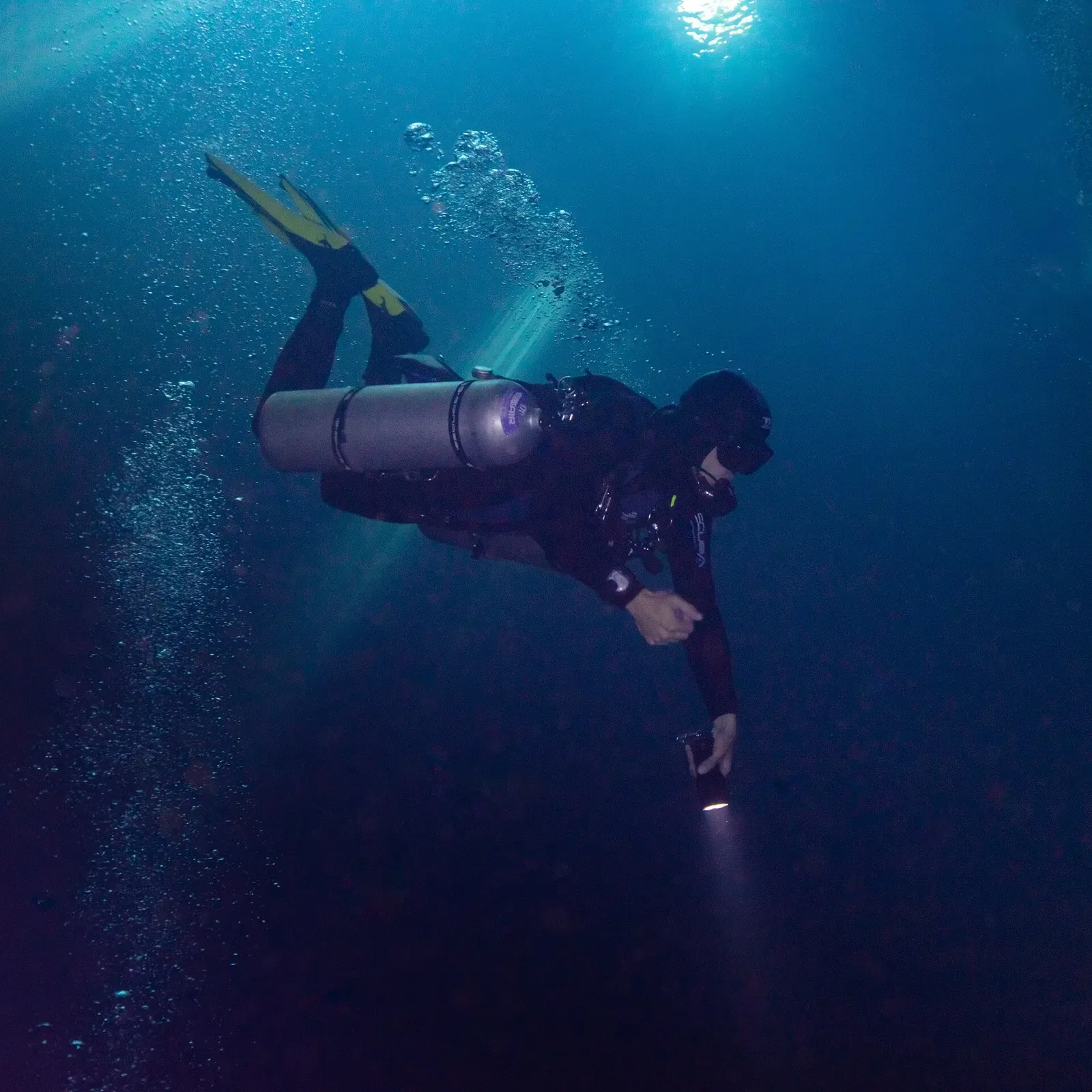 Diver finning through deep blue water with daylight coming from far above