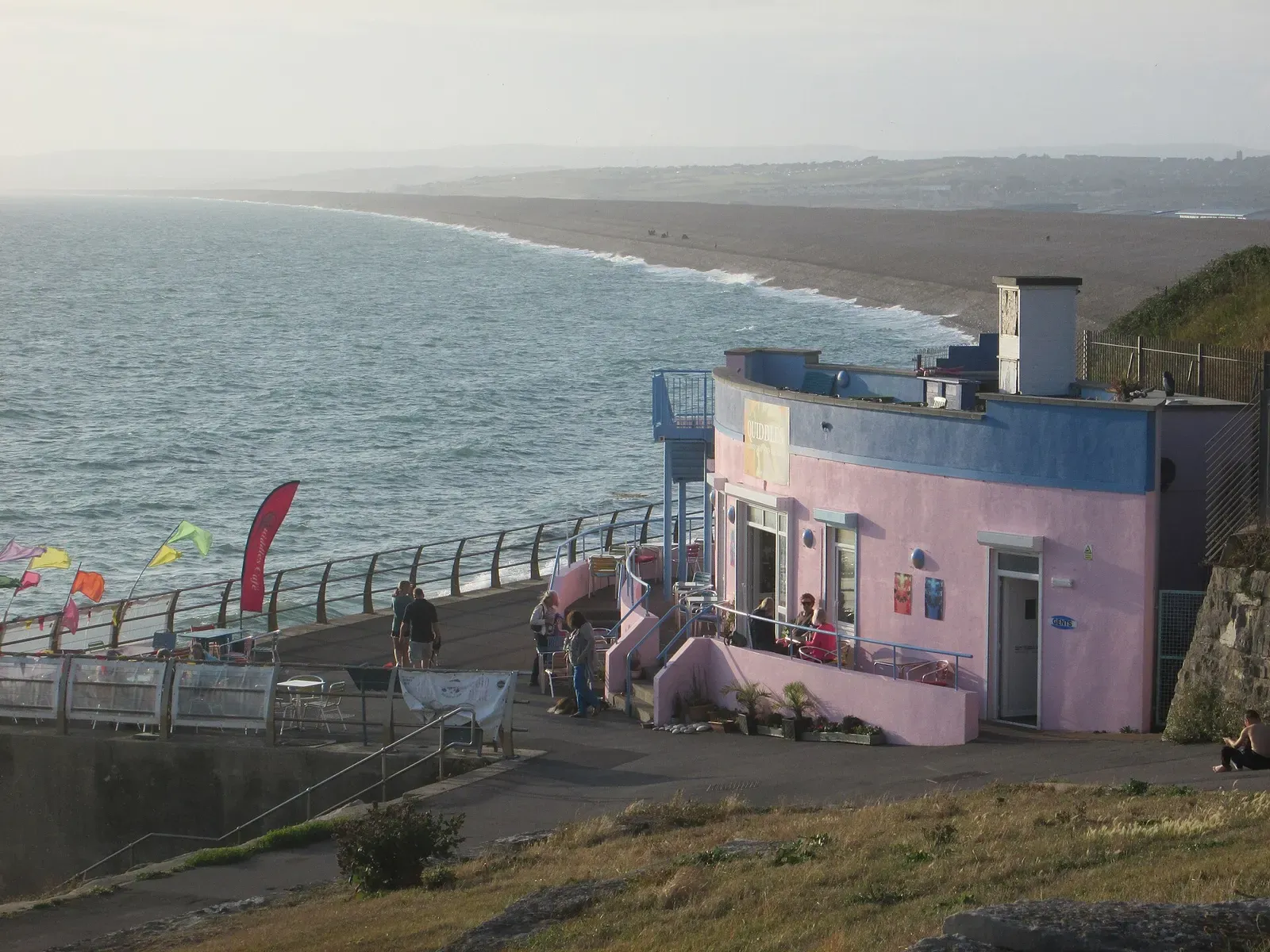 A pink café building above the sea wall and shingle beach at Chesil Cove