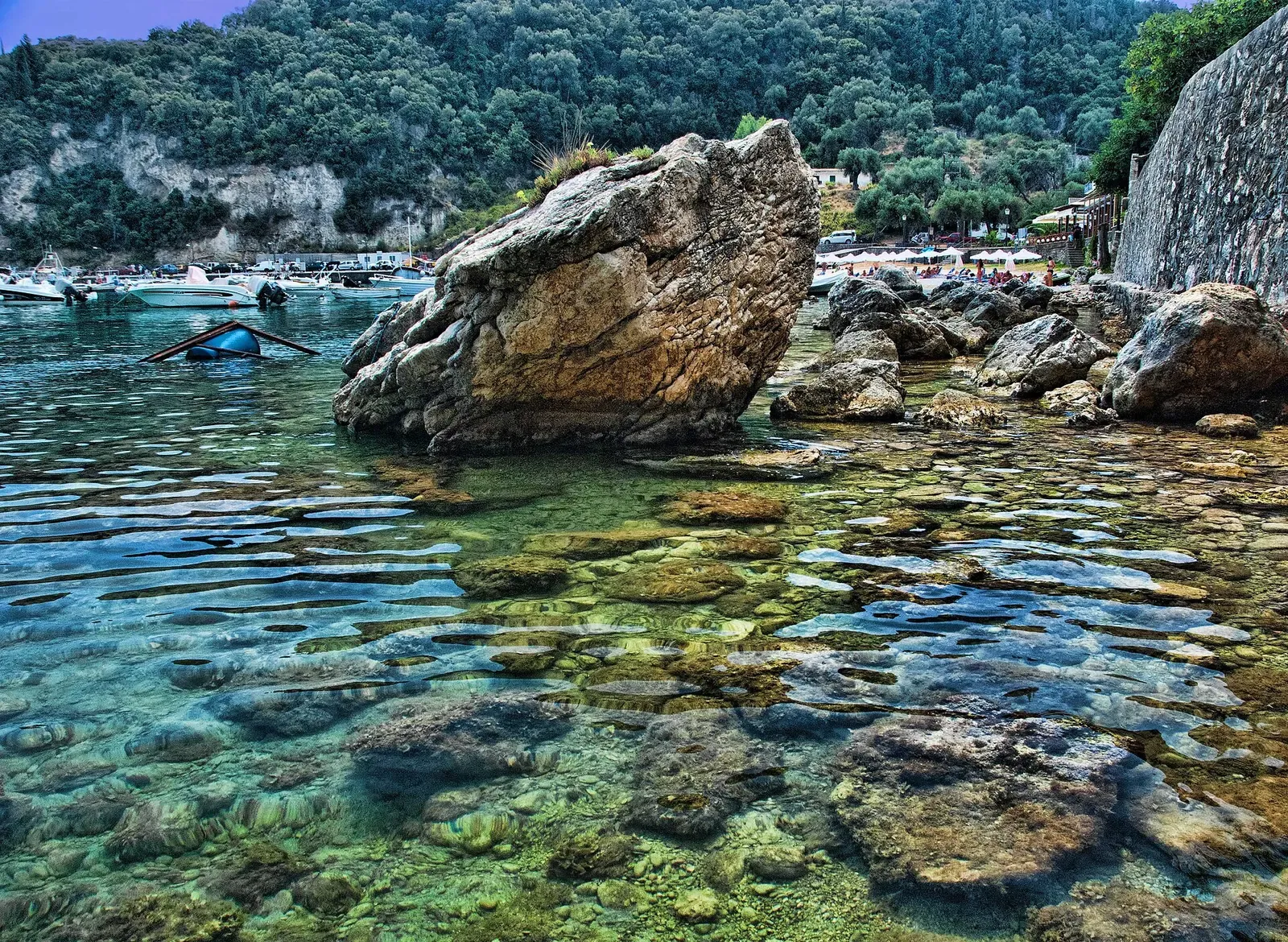 Shallow, clear water over a rocky, weed-covered seabed beside a large boulder at Palaiokastritsa.
