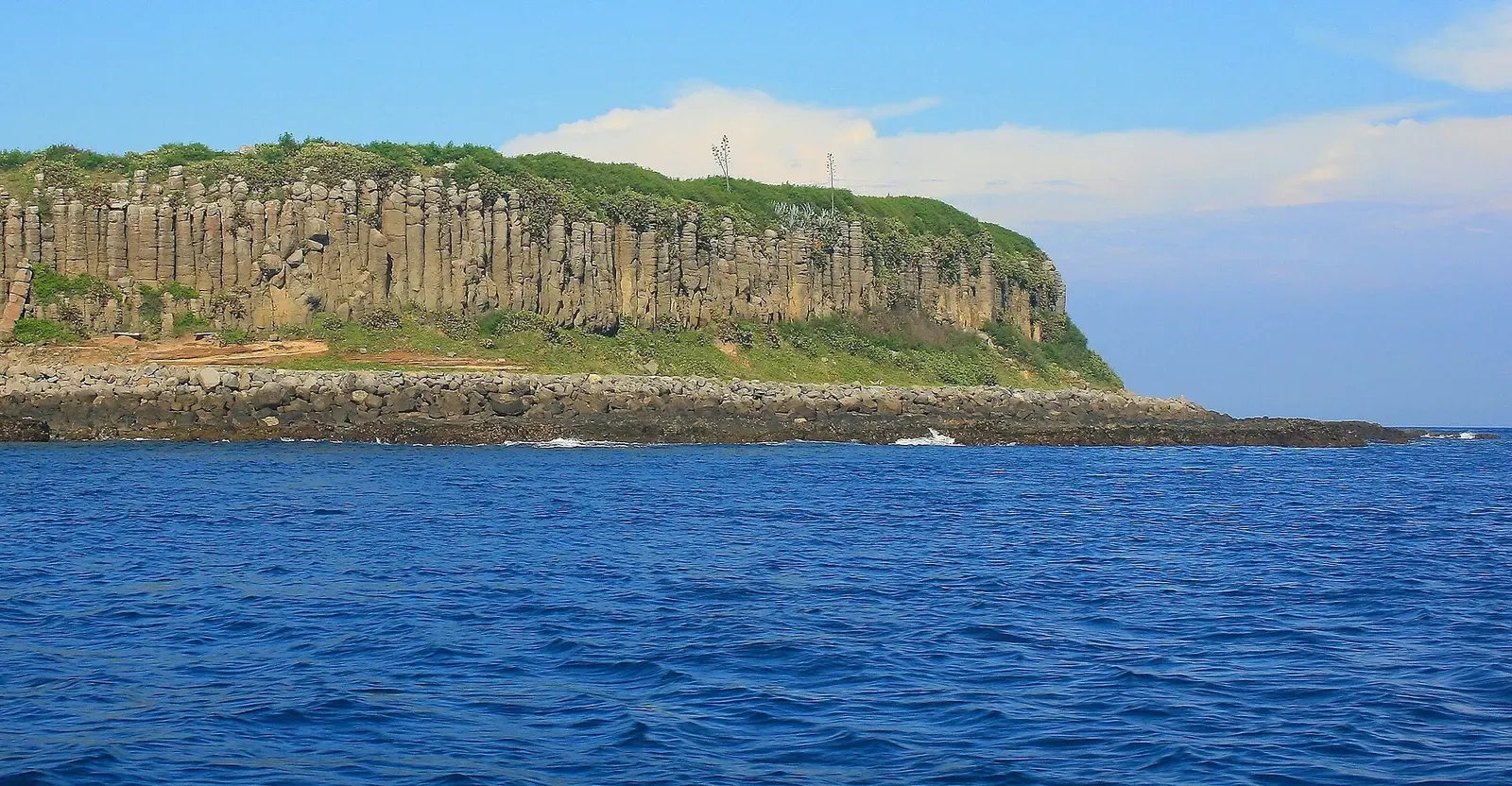 A low island edged with tall columnar basalt cliffs and a green top, seen across deep blue sea — Penghu Islands