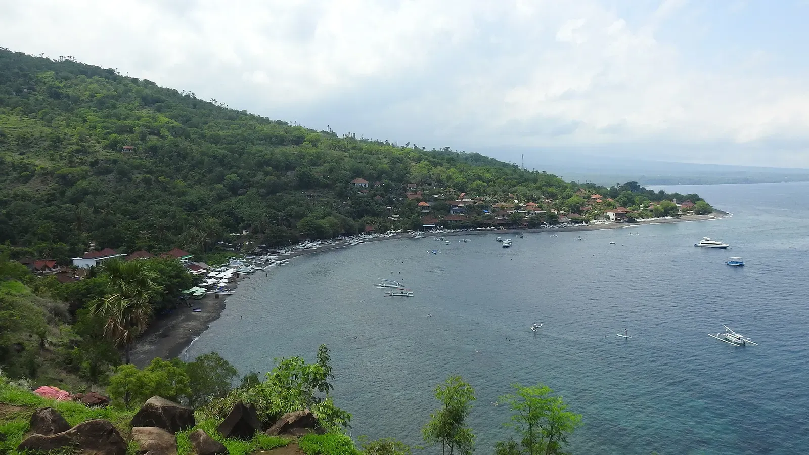 A wide bay with moored boats below a green hillside, seen from a cliff above the shore — Amed.