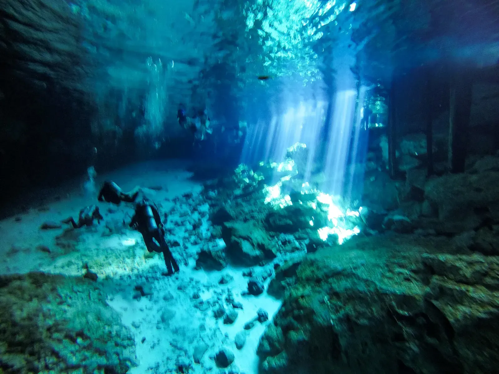 Cave diver descending through beams of sunlight inside a Yucatan cenote — Riviera Maya Cenotes