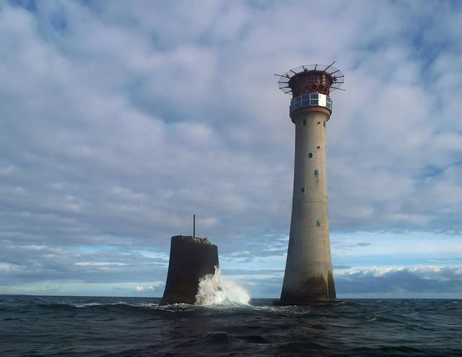 A tall granite lighthouse and the stump of an older tower rise from the sea under a cloudy sky — Eddystone, Plymouth Sound & HMS Scylla