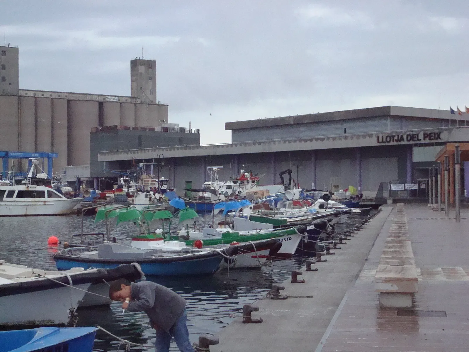 Fishing boats moored at the El Serrallo quay in Tarragona's port, with warehouse buildings behind
