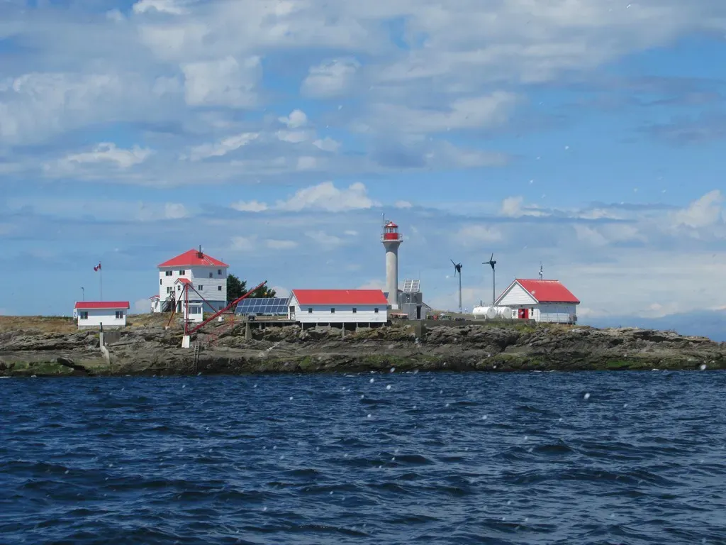 A small rocky island topped by white buildings with red roofs and a white lighthouse tower, surrounded by choppy blue water — Nanaimo & Gabriola Island.