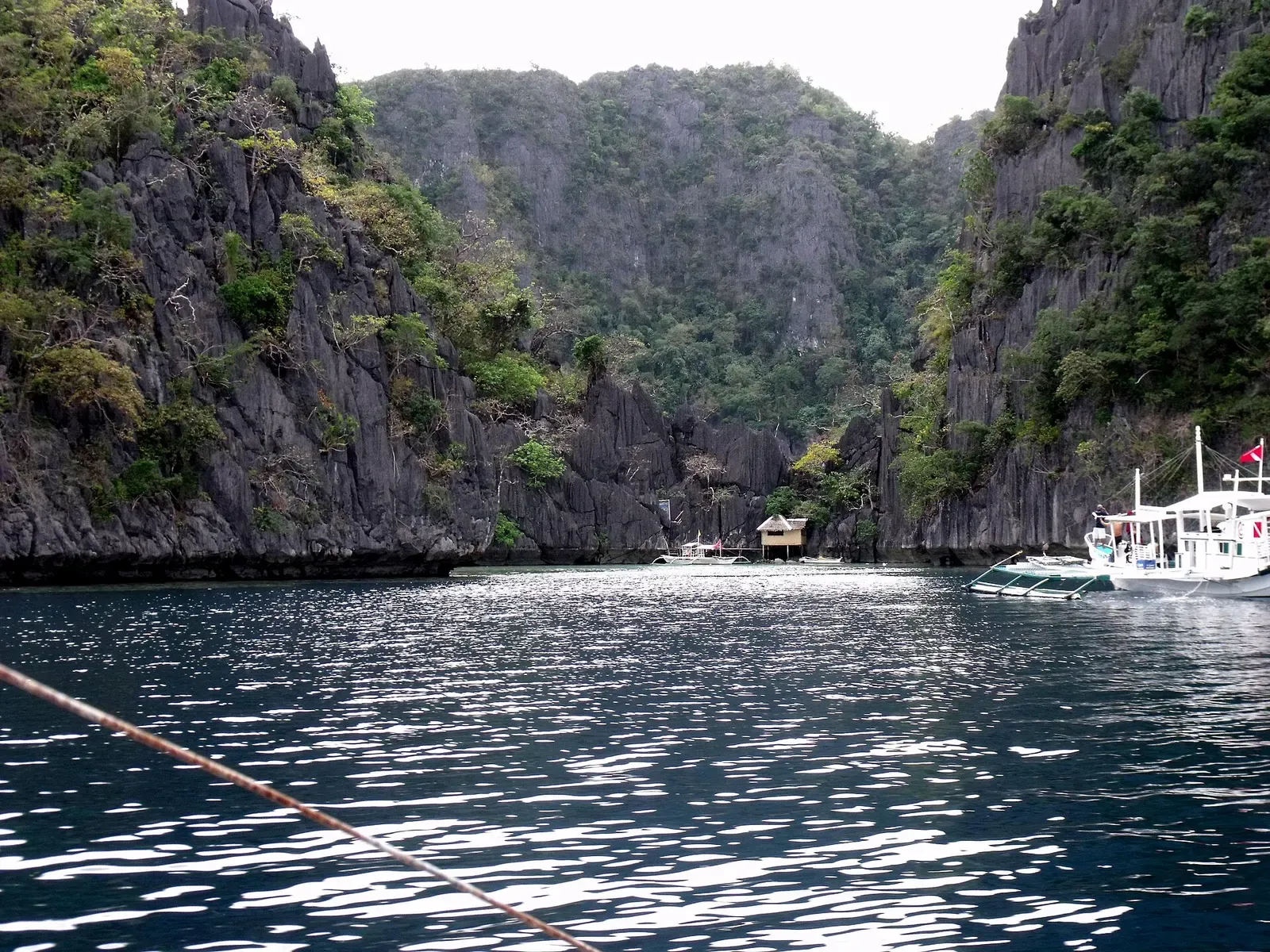 Calm entrance lagoon leading toward Barracuda Lake, flanked by tree-topped limestone cliffs — Coron