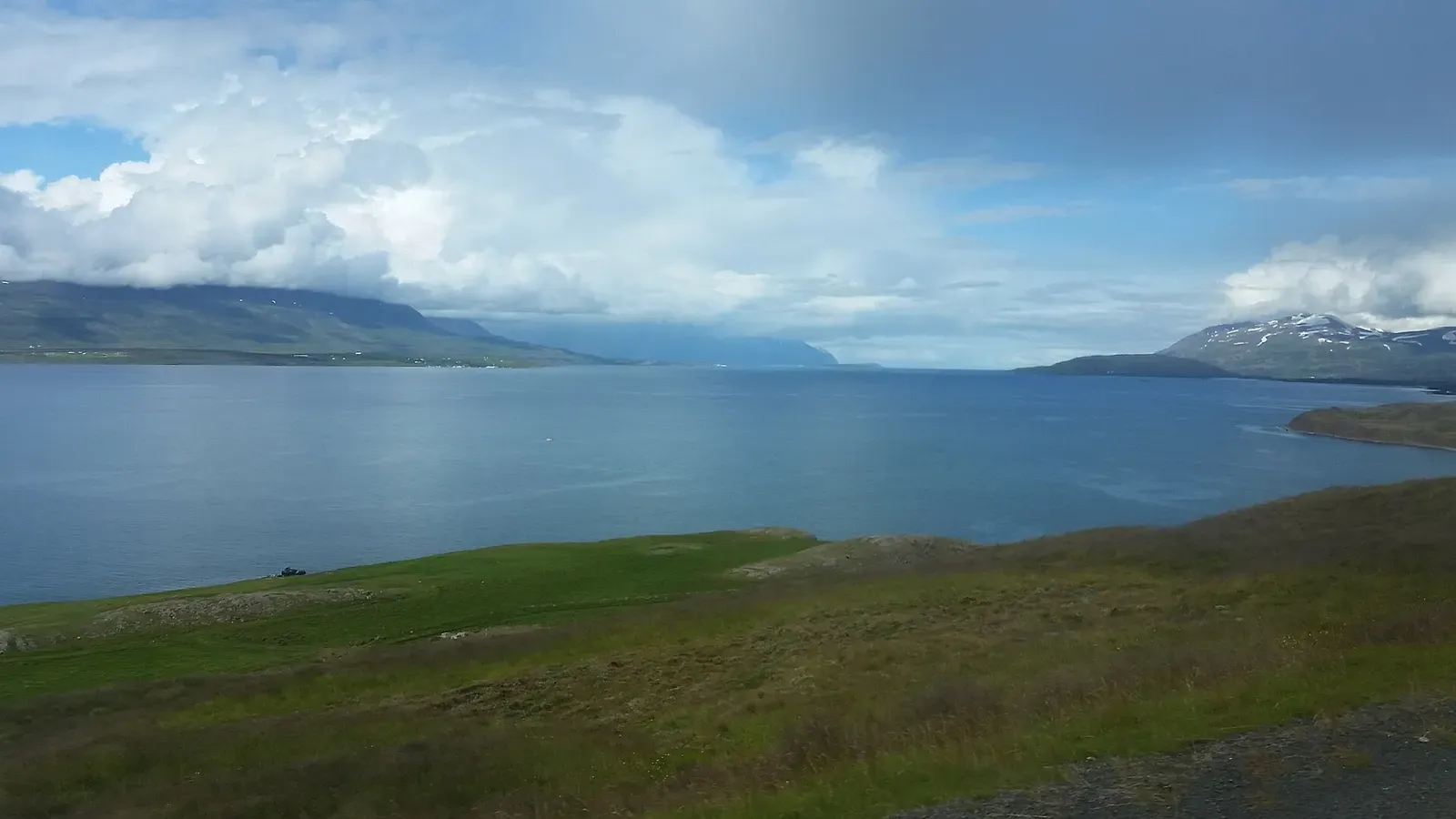 Sunlit peaks frame the wide blue waters of Eyjafjörður fjord under a partly clouded sky — Strýtan