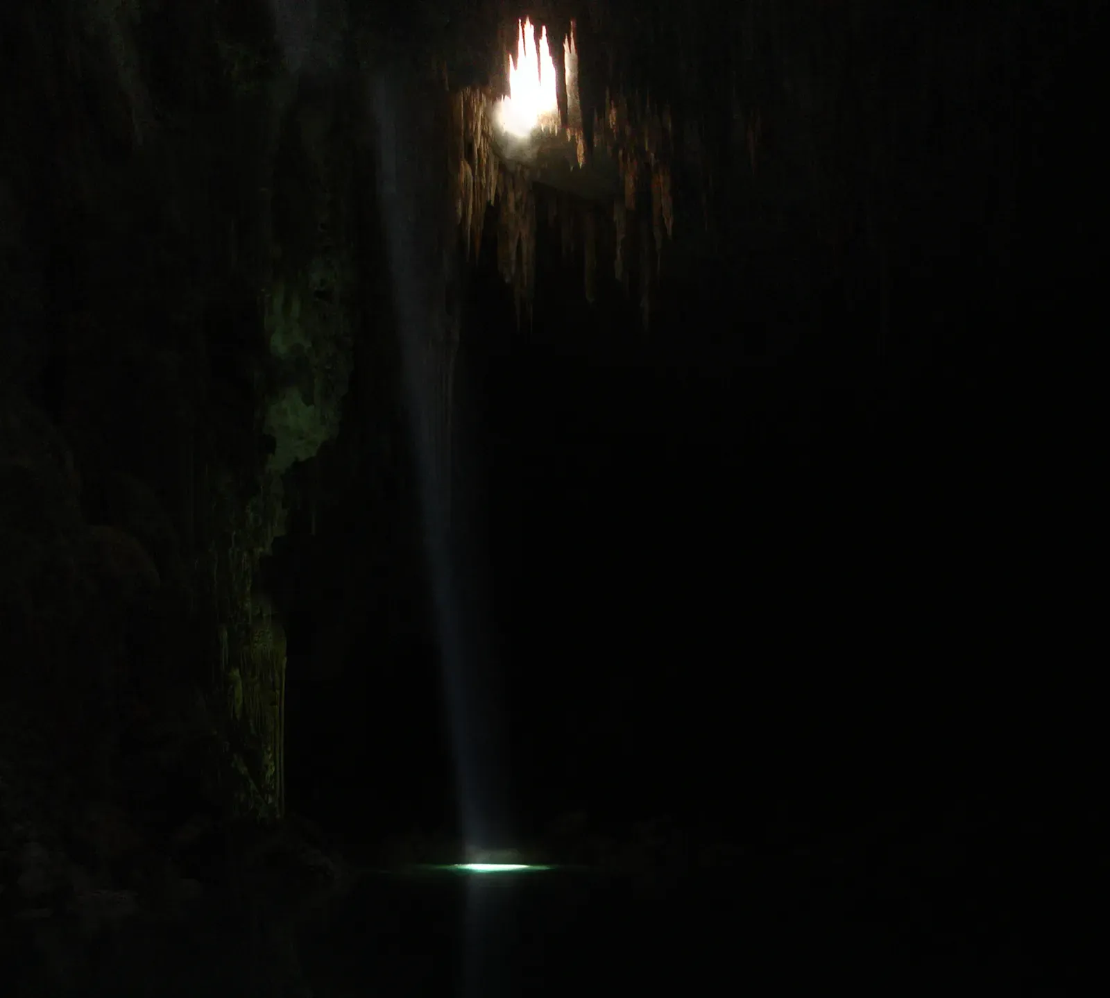 A single column of light cutting through the dark, cavernous chamber of Abismo Anhumas — Bonito