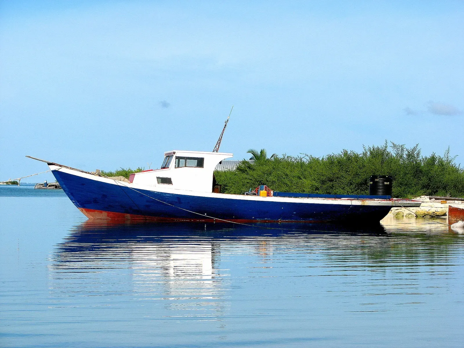 A blue and white fishing boat anchored on flat water at Hithadhoo harbour — Addu Atoll