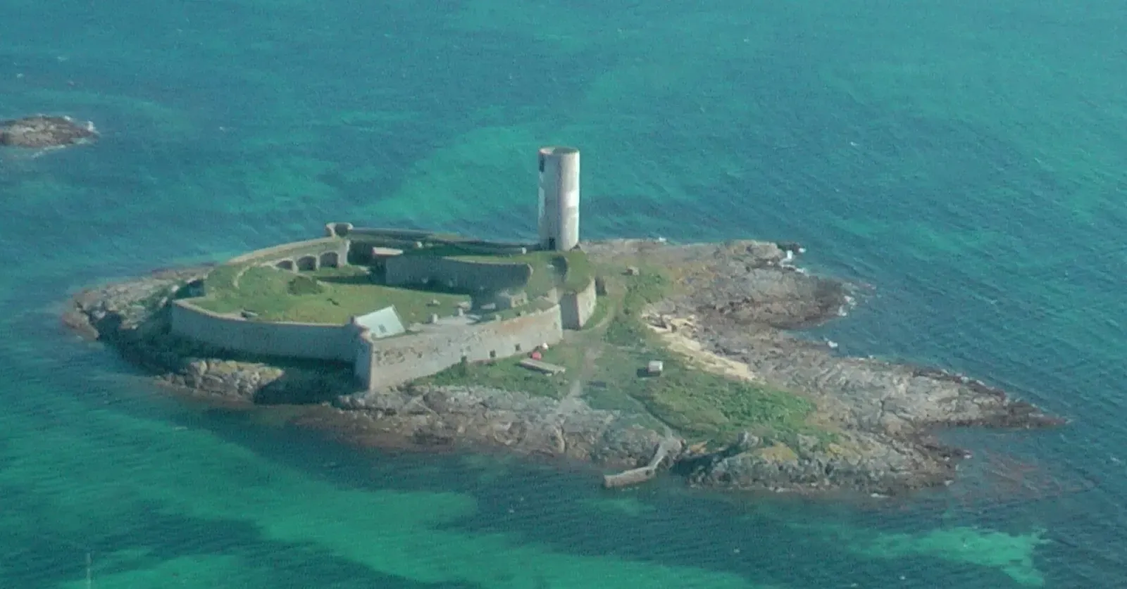 Aerial view of a walled stone fort with a round tower on a rocky islet, surrounded by green shallows and deeper water — Glénan Archipelago