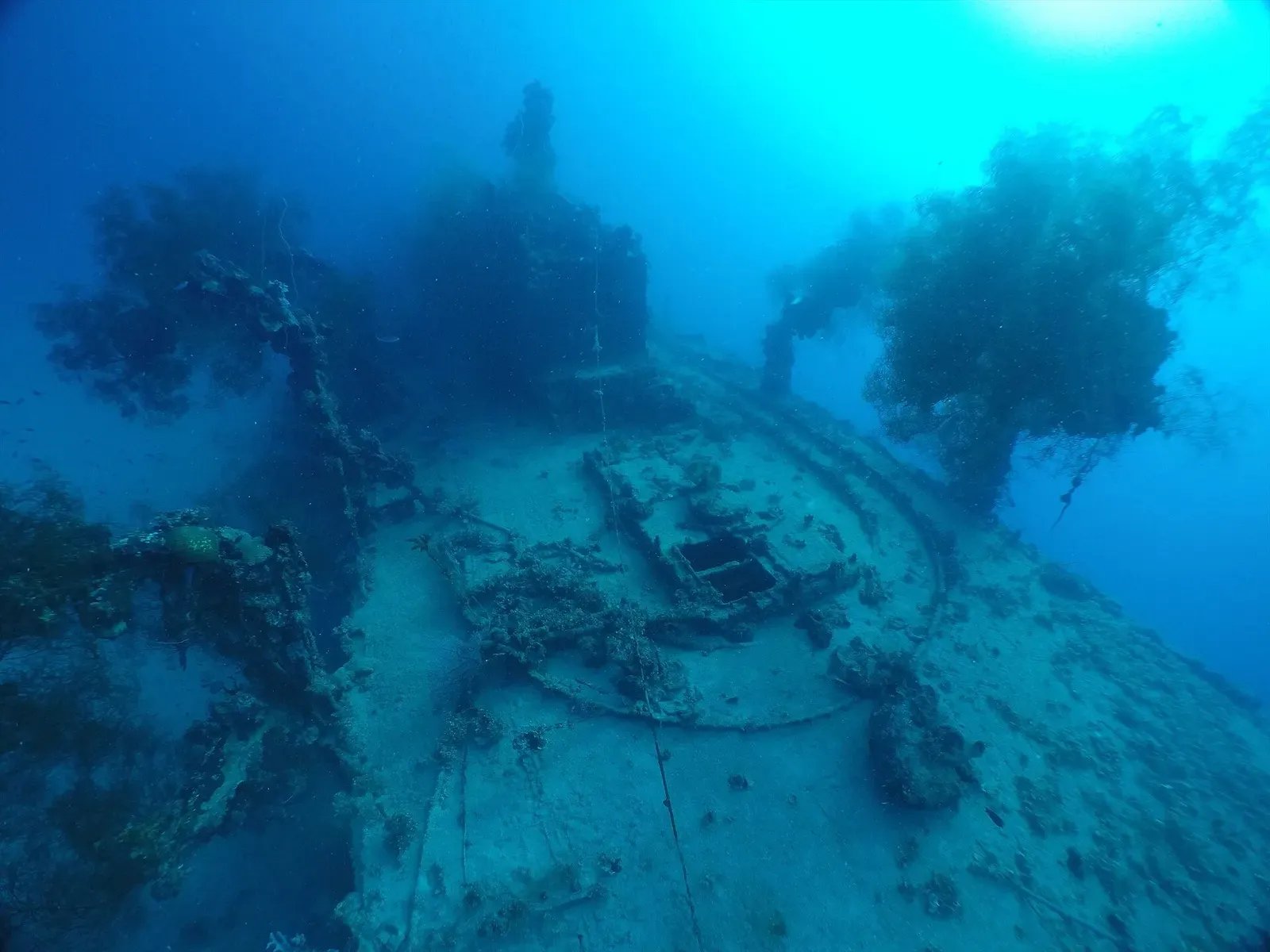 A wreck deck with fittings and growth slopes away under bright blue water, with sunlight above — Fumizuki, Chuuk Lagoon.