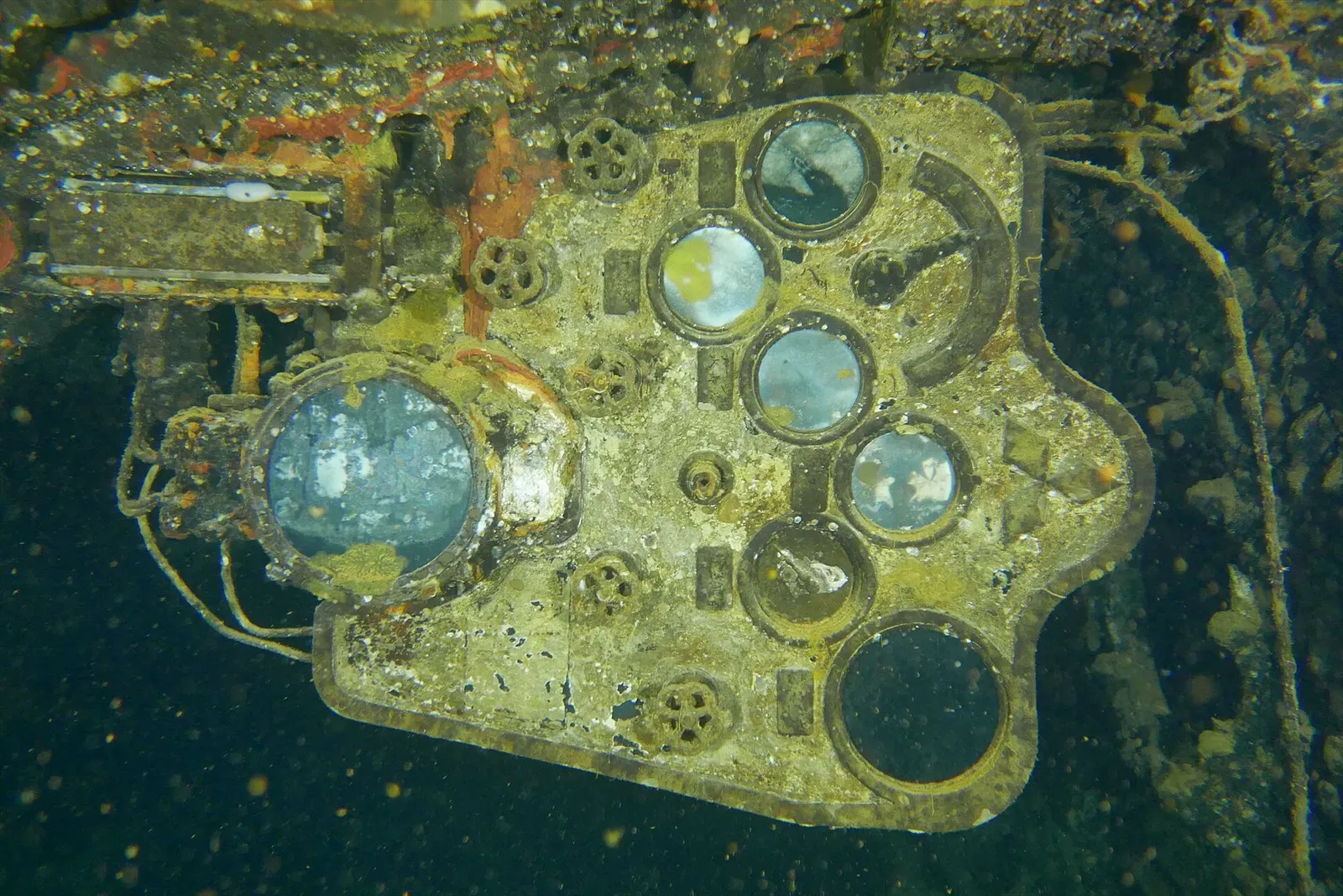 A wreck control panel with round glass gauges and valve wheels, crusted and lit by a torch — Kiyosumi Maru, Chuuk Lagoon.