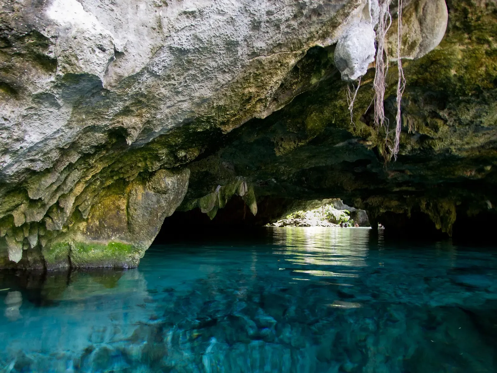 A stone archway frames a calm turquoise pool inside a limestone cave mouth — Gran Cenote, Riviera Maya Cenotes.