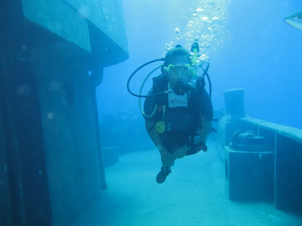 A diver hovers beside an open hatch on the hull of a sunken ship — Grand Cayman