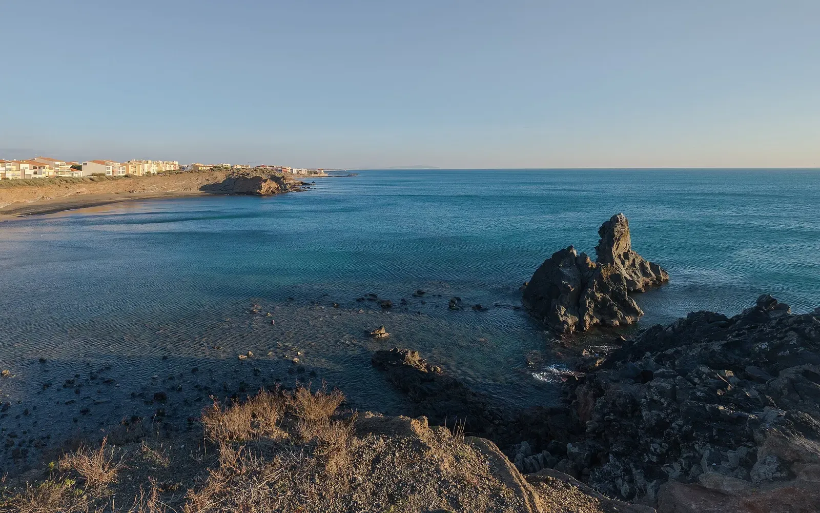 Dark rock outcrops break the surface of clear water in the Grande Conque cove