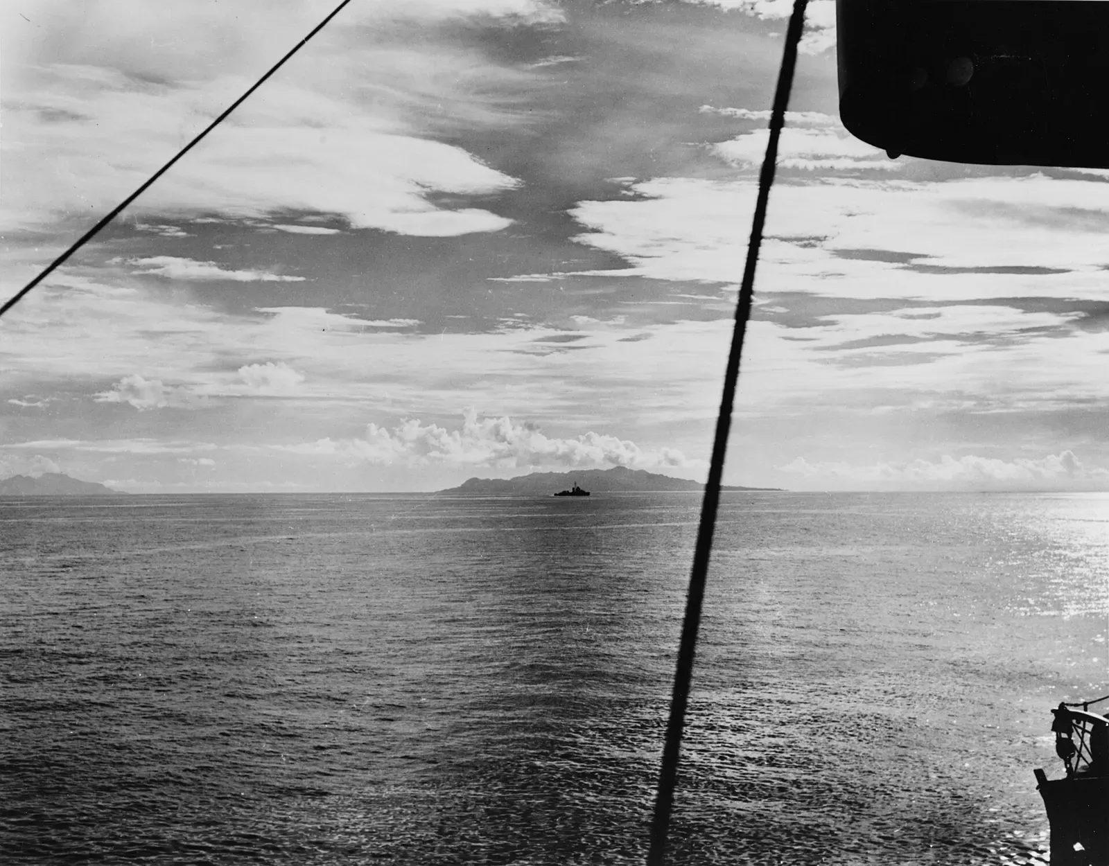 Black-and-white view from a warship over a flat sea to a lone destroyer and a mountainous island on the horizon — Iron Bottom Sound