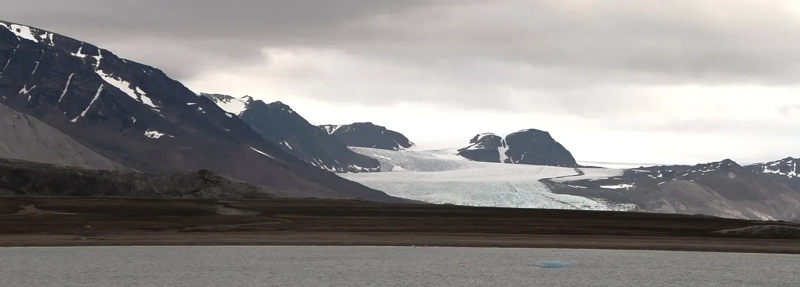 Conwaybreen glacier descends to the shore of Kongsfjorden, a small cabin visible in the foreground — Svalbard.