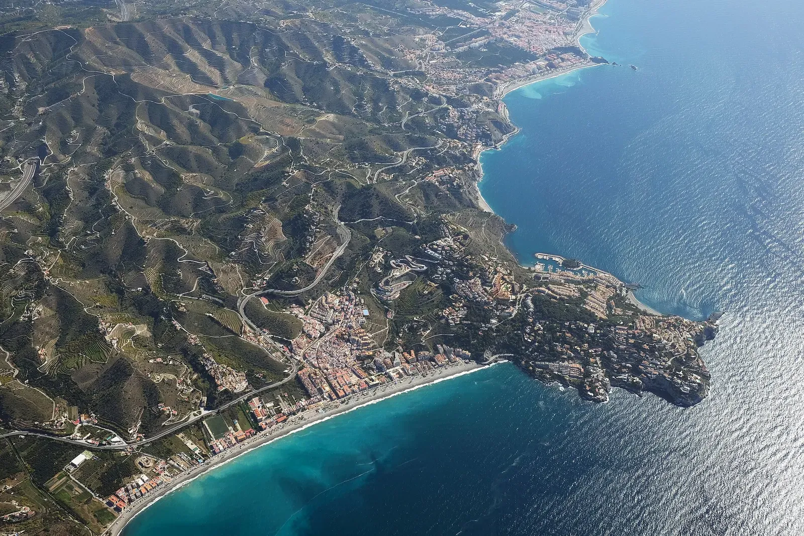 Aerial view of La Herradura's curved bay and terraced coastal hills.