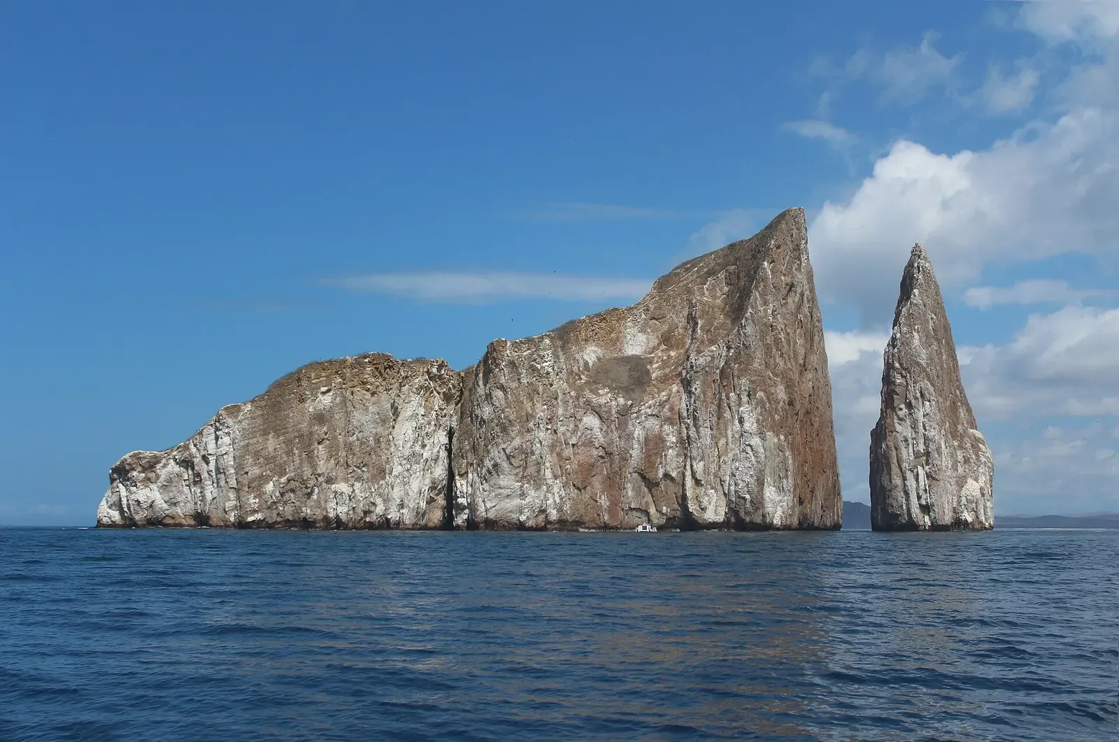 A tall flat-topped rock and a separate narrow spire rising from calm blue sea under a clear sky — Kicker Rock, Galápagos