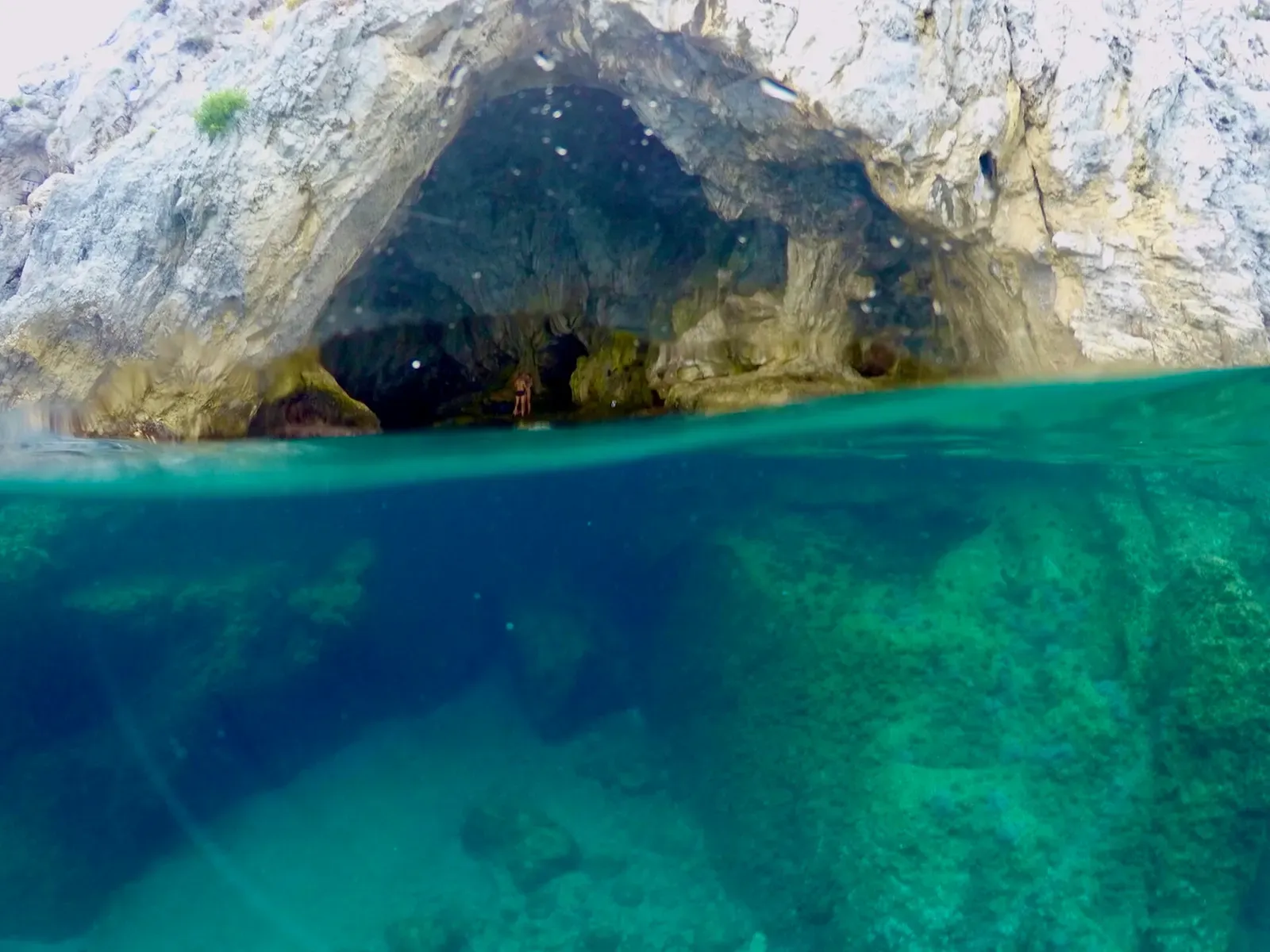 Over-under view of a rock-ceilinged marine cave in Bergeggi, its shape reflected in turquoise water
