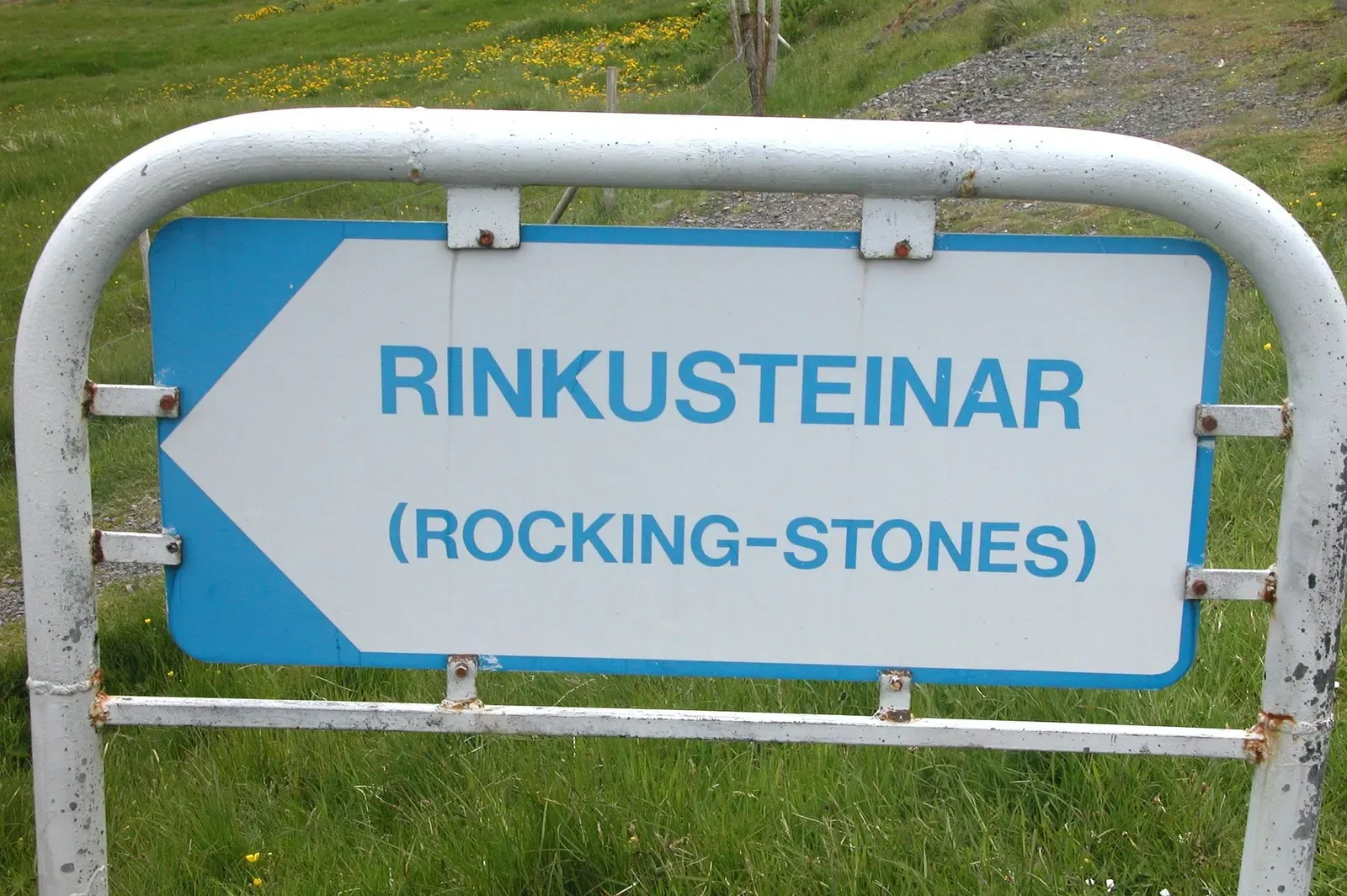 Blue trailhead sign reading 'RINKUSTEINAR (Rocking-Stones)' beside the road into Oyndarfjørður — The Rocking Stones in Oyndarfjørður, Faroe Islands