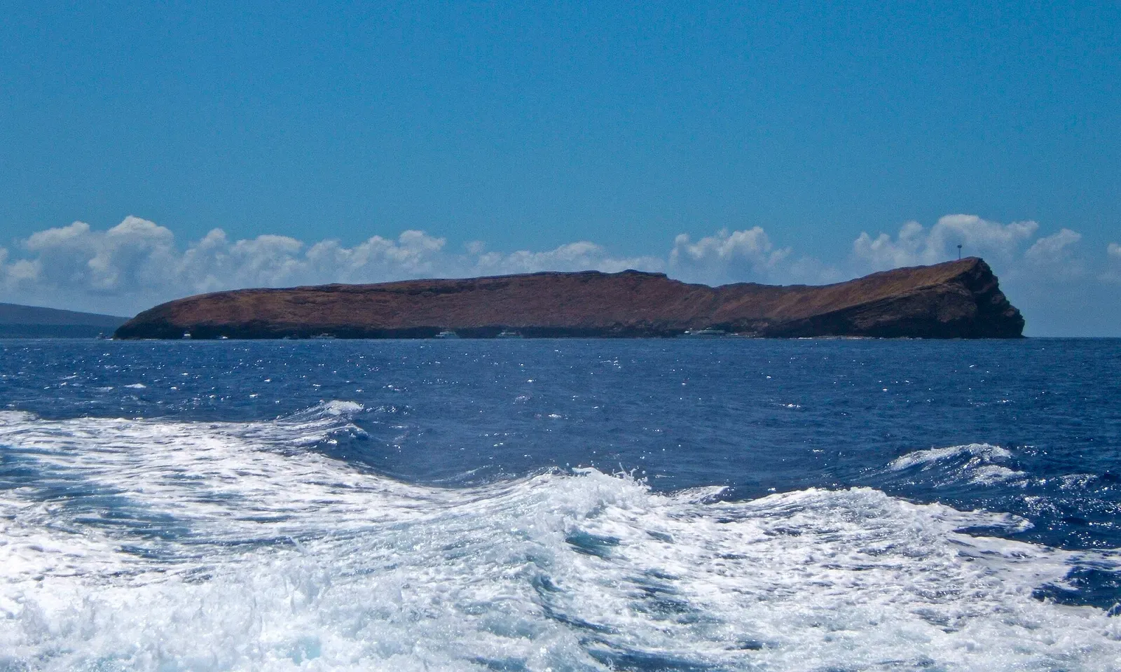Molokini's crescent islet seen at boat level from the wake of a departing vessel — Molokini Crater