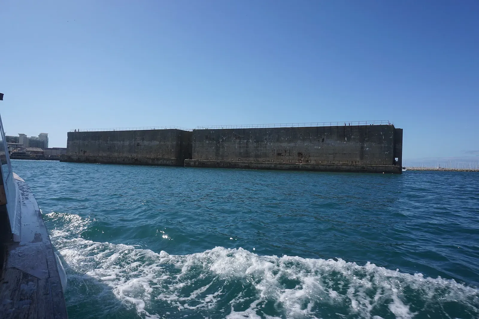 A long concrete breakwater wall with waves breaking against it in Portland Harbour