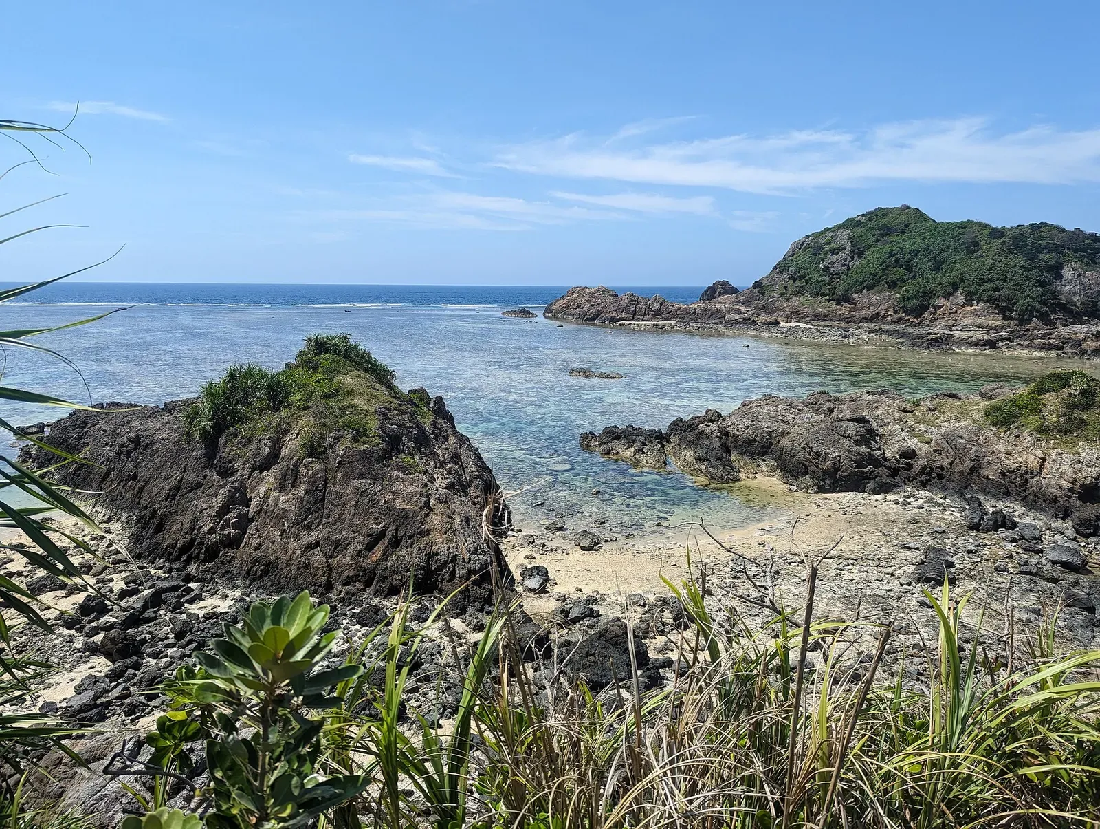 Rocky green promontory jutting into a shallow turquoise lagoon with scattered coral rock — Manta Scramble, Ishigaki