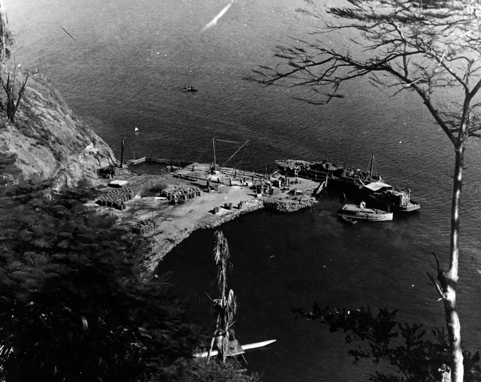 1943 black-and-white aerial photo of a wooden jetty and boats in a steep-sided New Guinea inlet — Tufi
